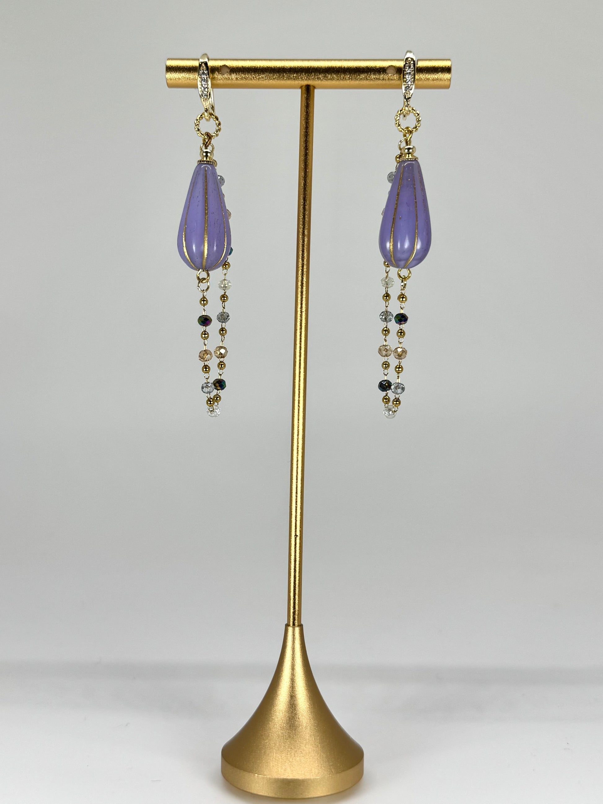 Purple earrings with gold accents on a gold stand against a white background