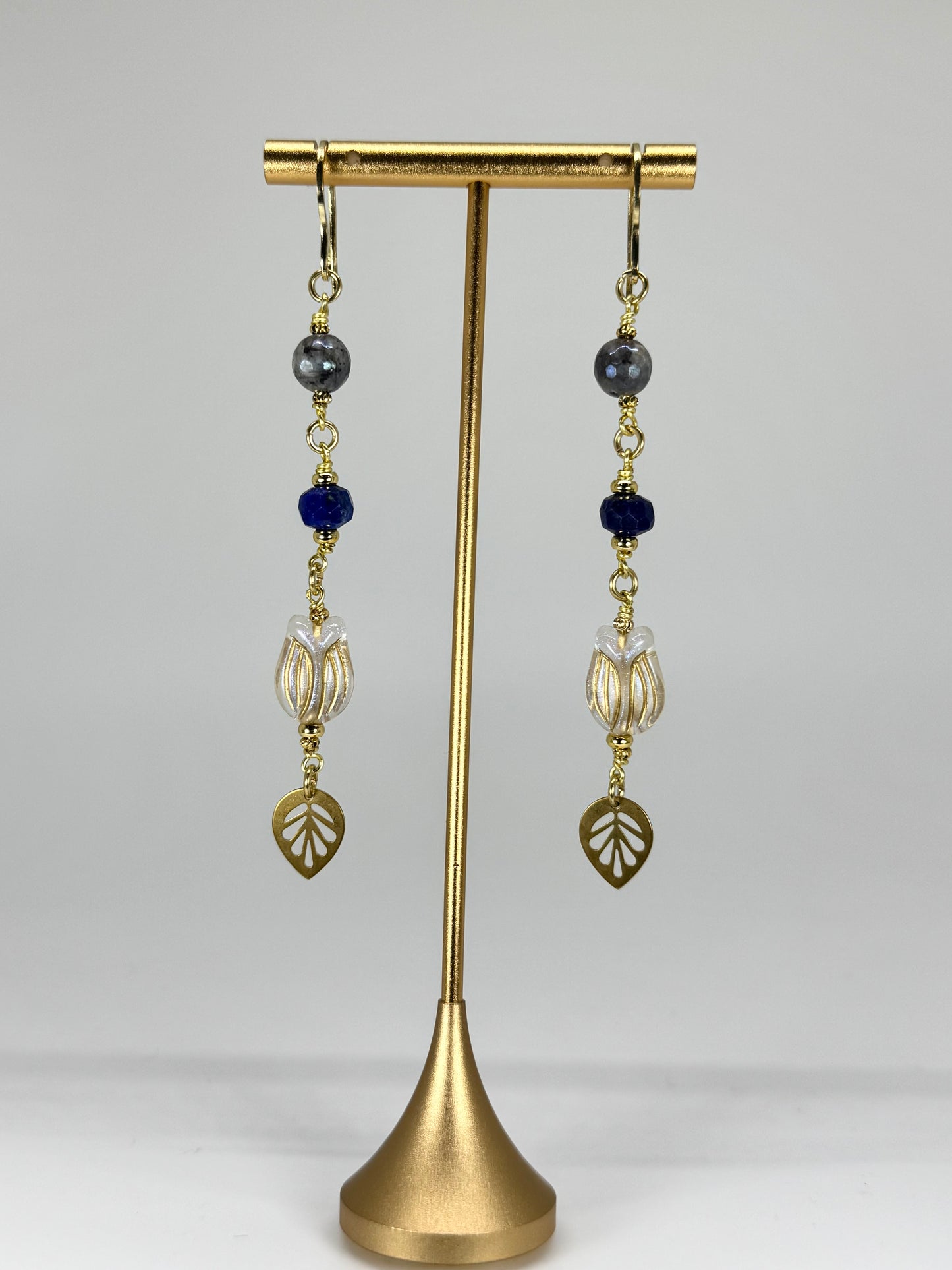 Pair of earrings with leaf and bead design on a gold stand against a white background