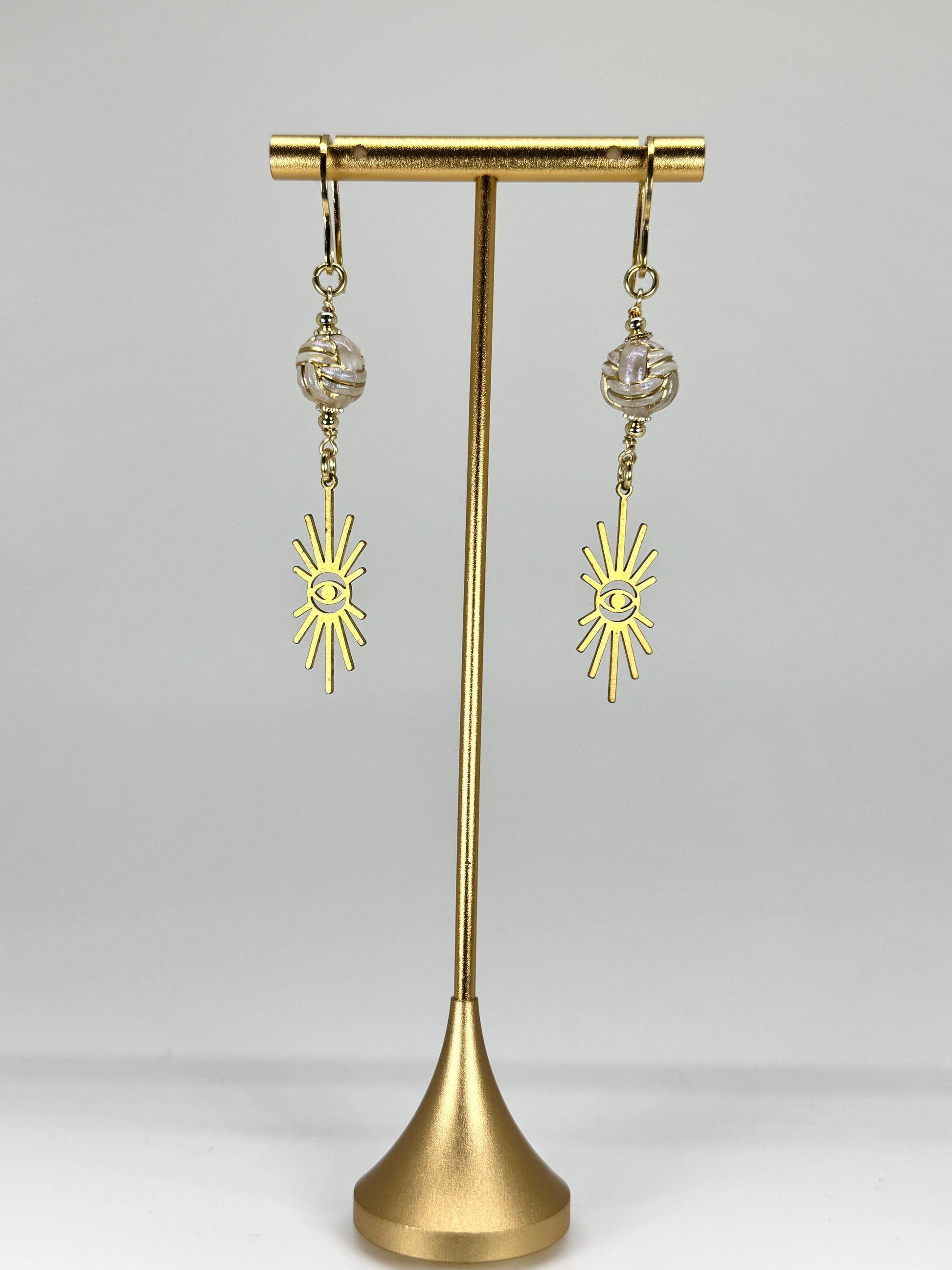 Gold earrings with sun designs on a gold stand against a white background