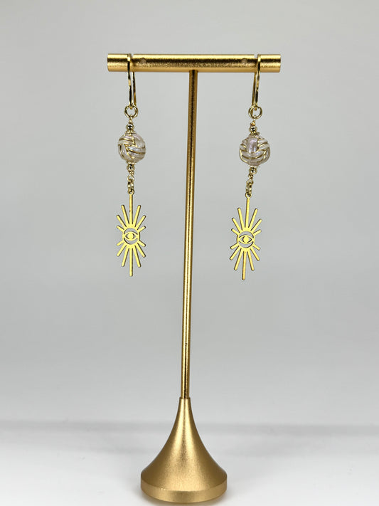 Gold earrings with sun designs on a gold stand against a white background