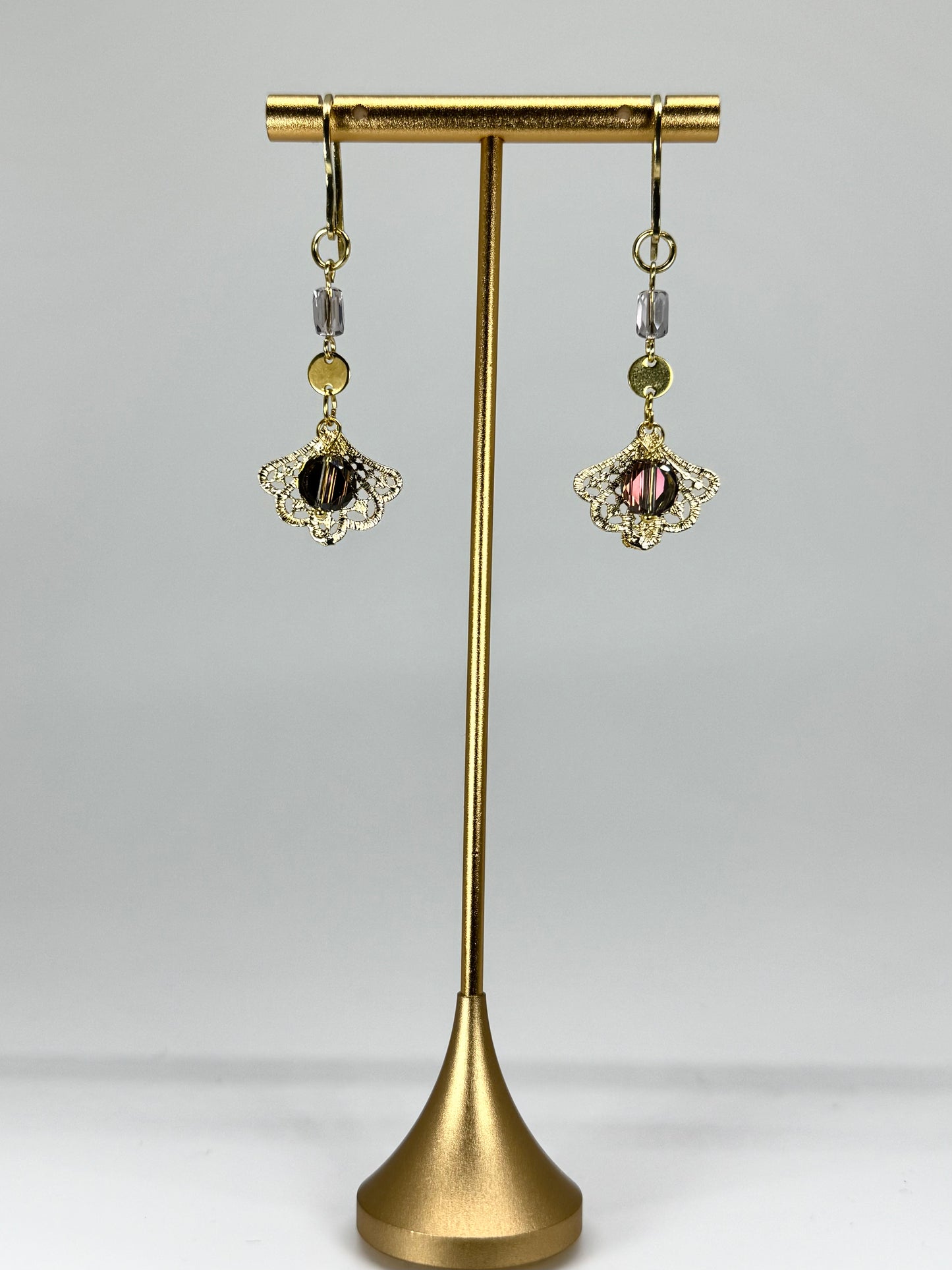 Pair of earrings on a gold stand against a gray background