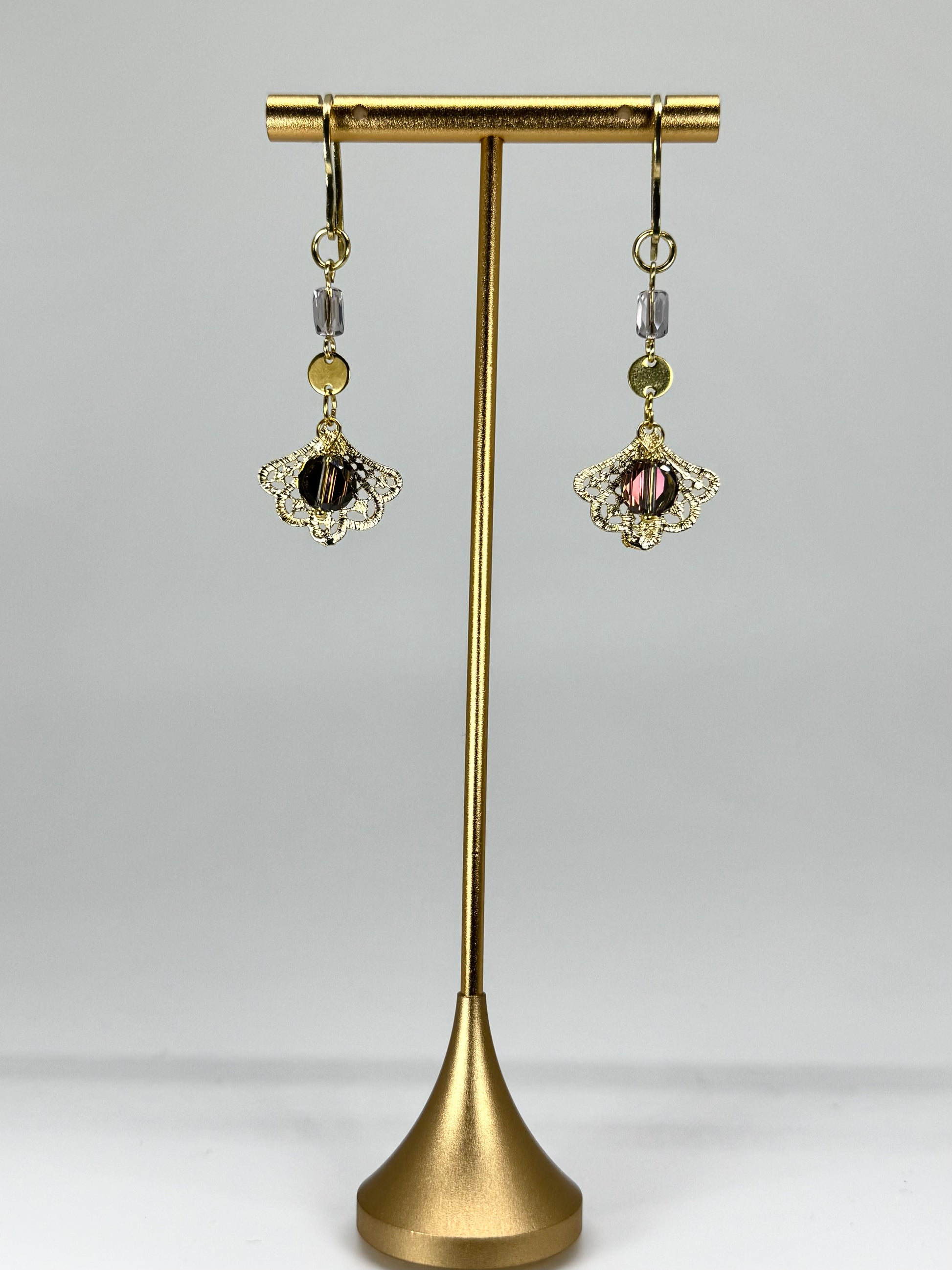 Pair of earrings on a gold stand against a gray background