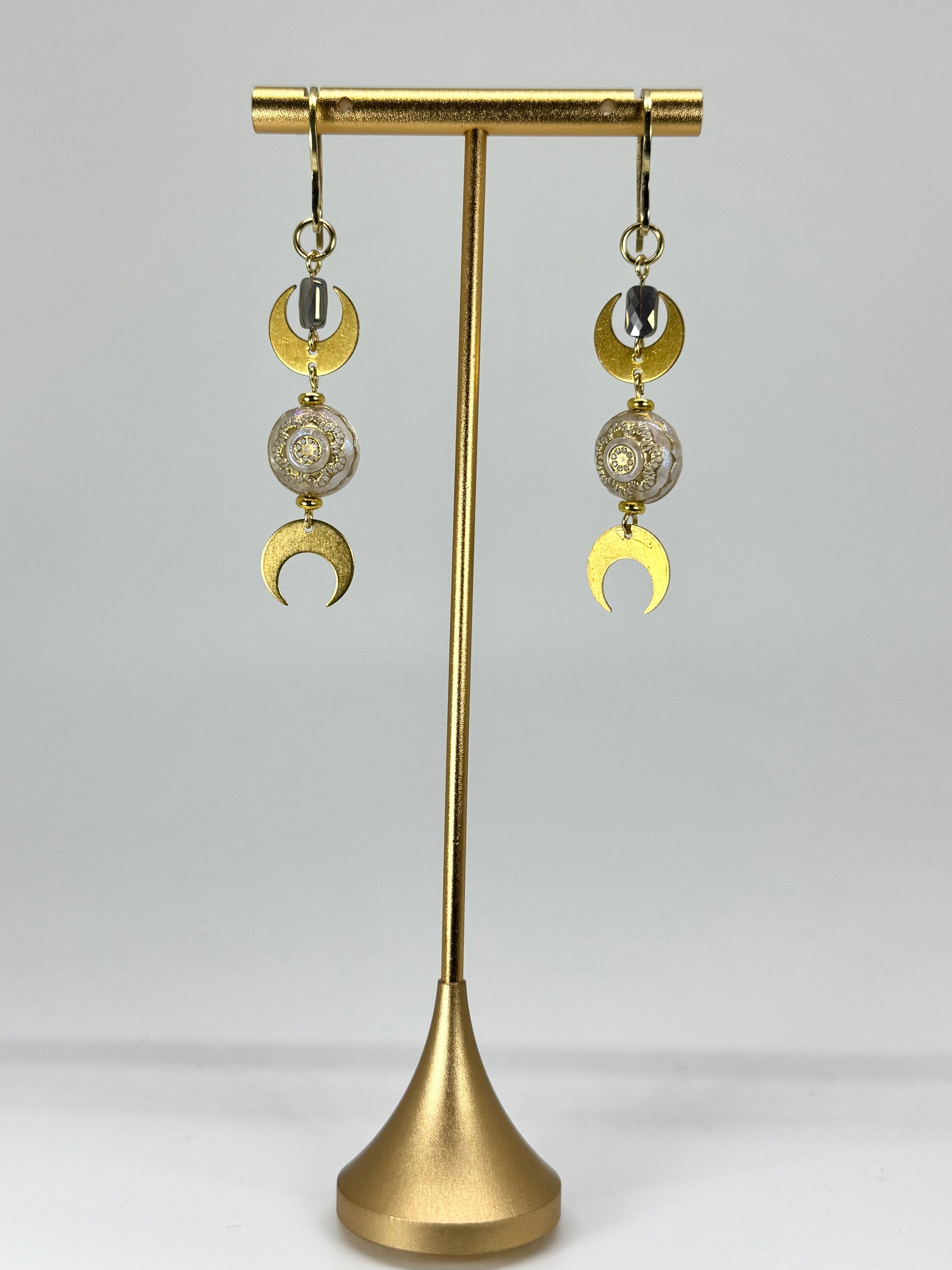 Gold earrings with intricate designs on a gold stand against a white background