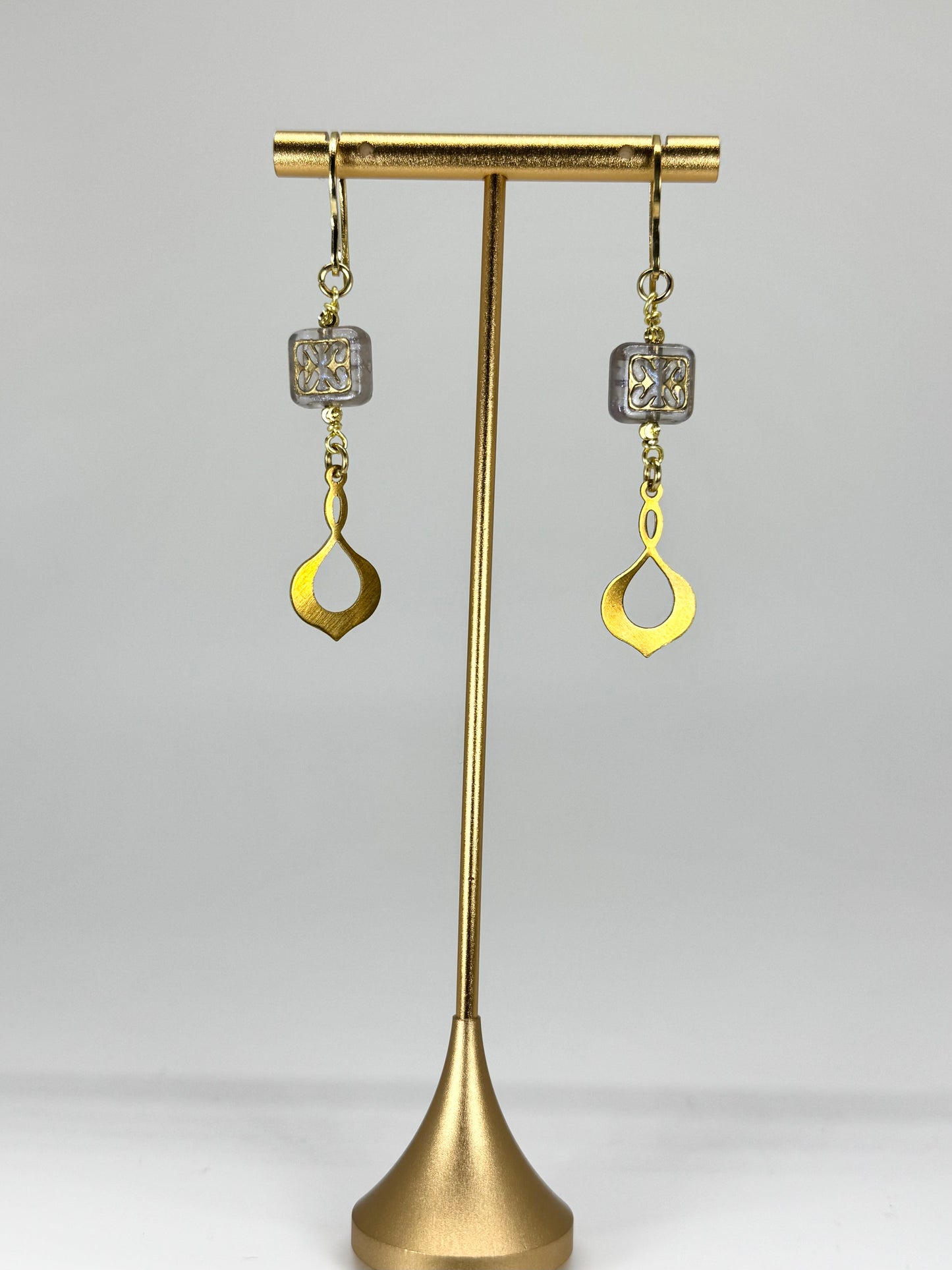 Gold earrings on a brass stand against a white background
