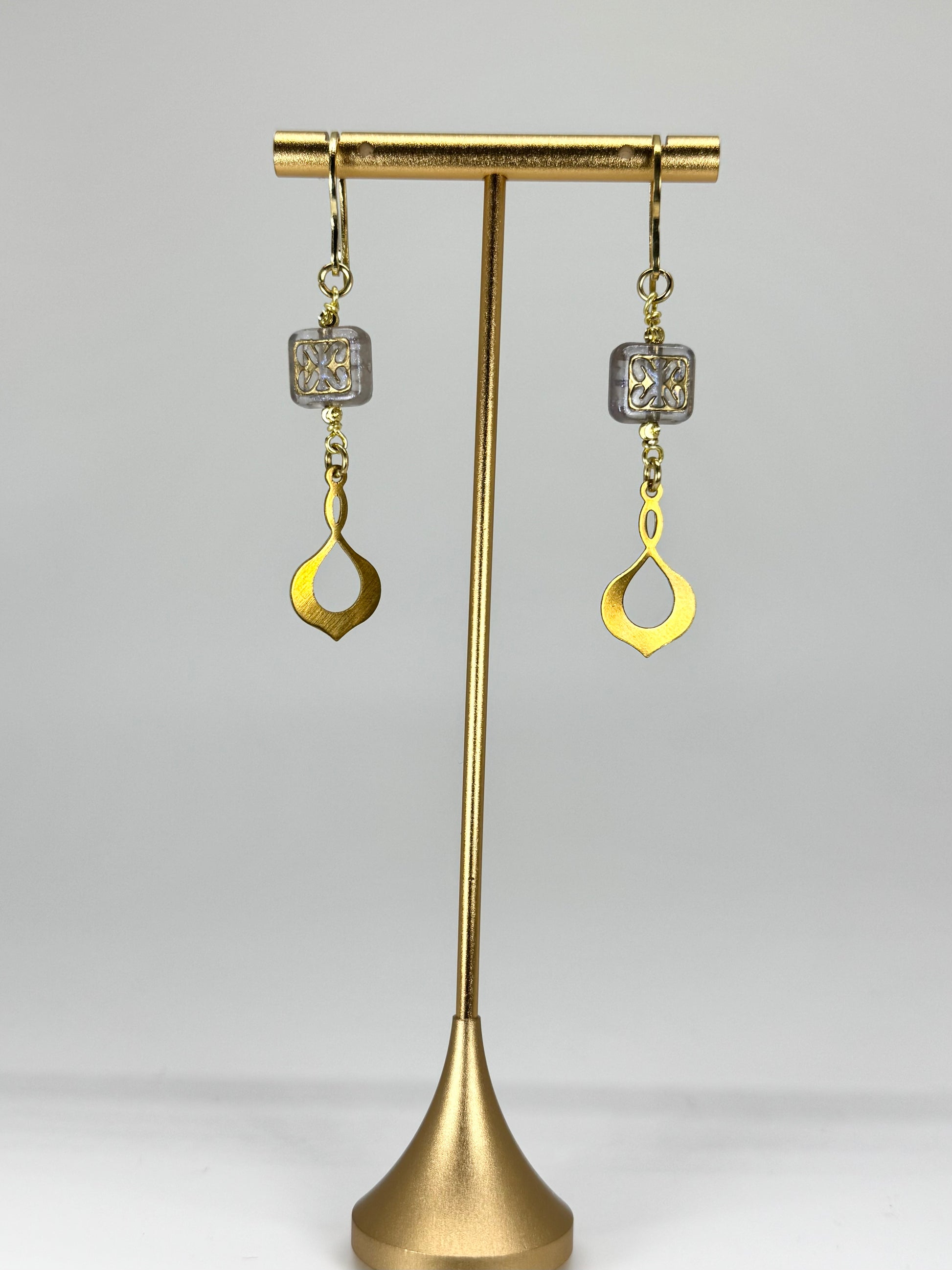 Gold earrings on a brass stand against a white background