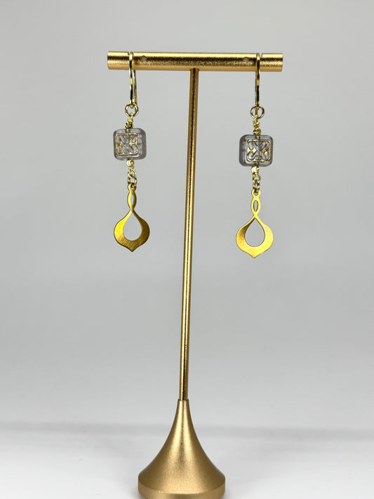 Gold earrings on a brass stand against a white background