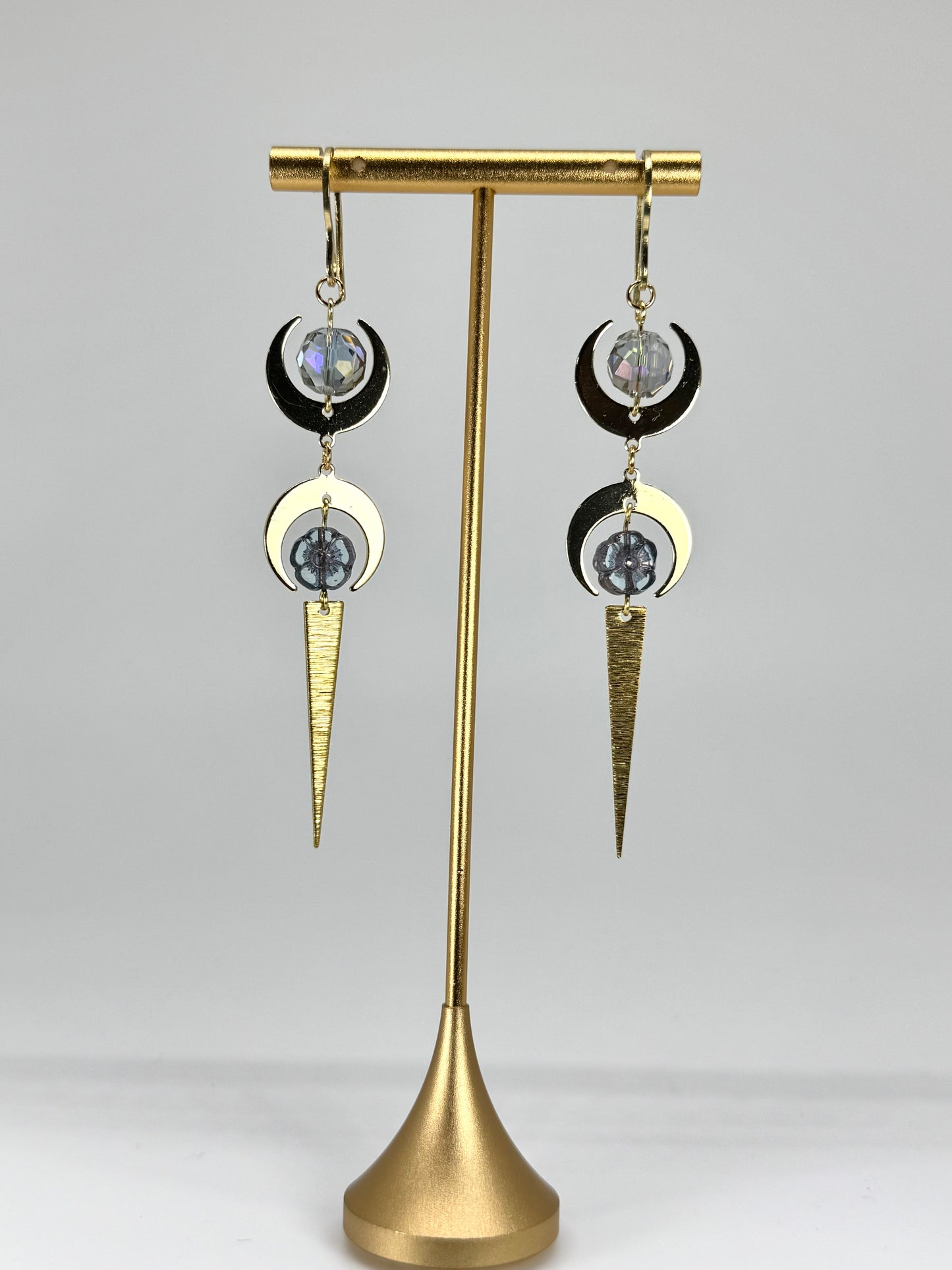 Pair of earrings on a gold stand against a gray background