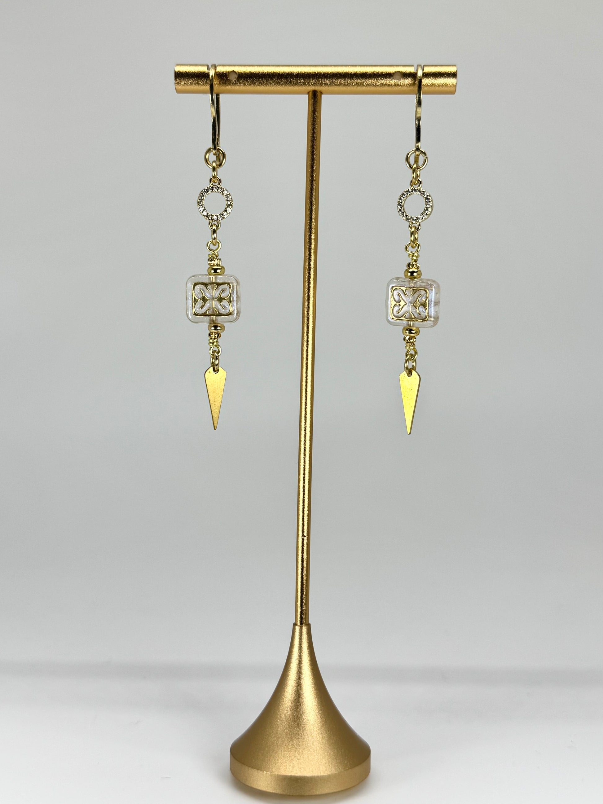 Gold earrings with triangular pendants on a gold stand against a gray background