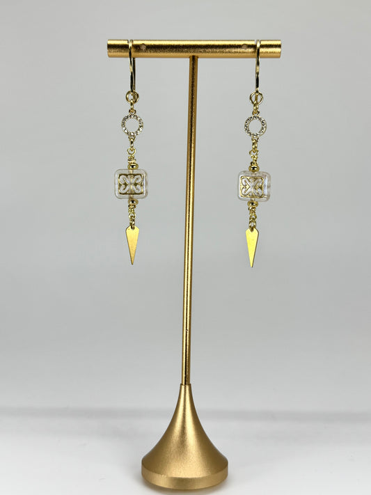Gold earrings with triangular pendants on a gold stand against a gray background