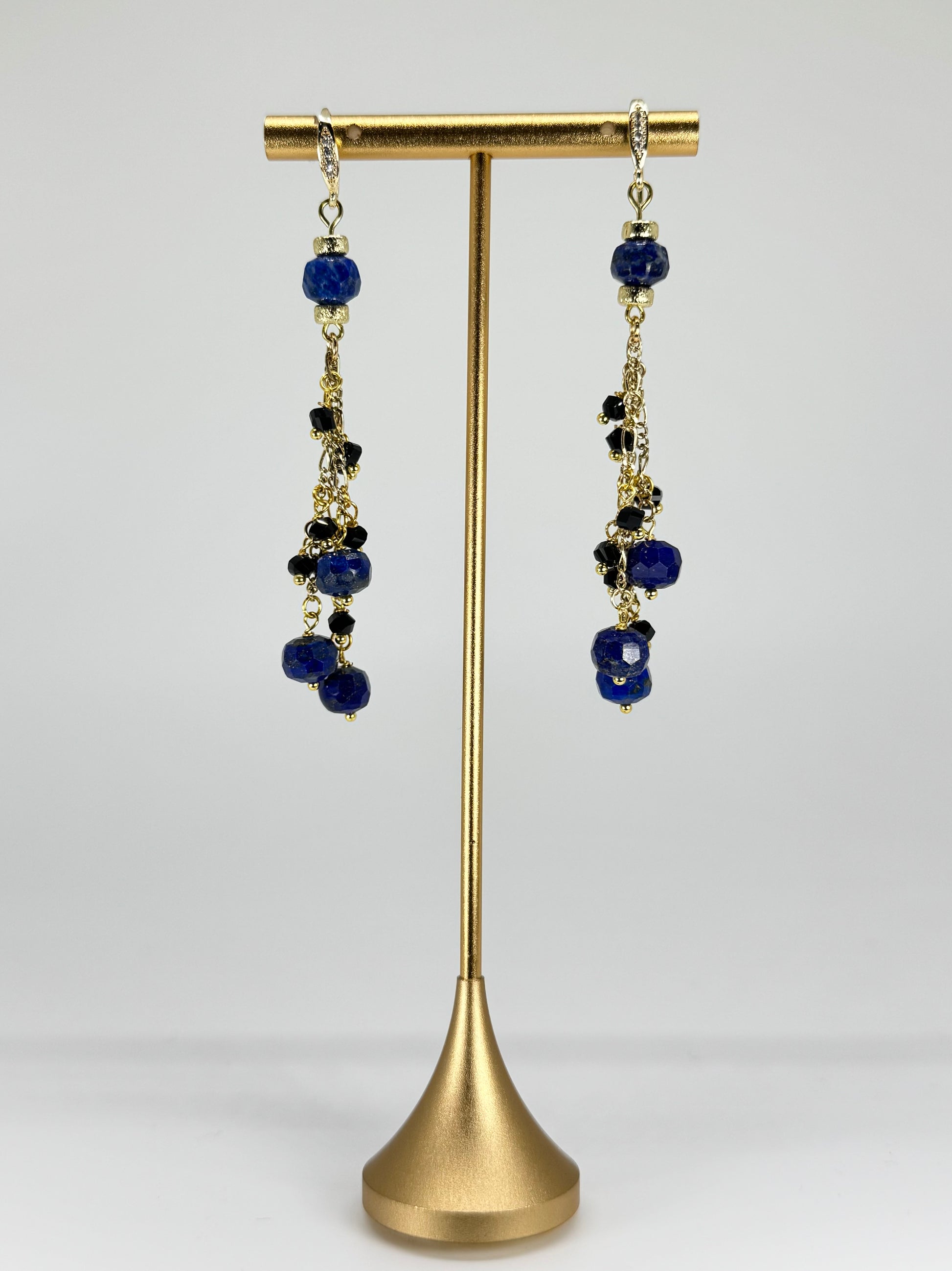 Pair of earrings with blue beads on a gold stand against a white background