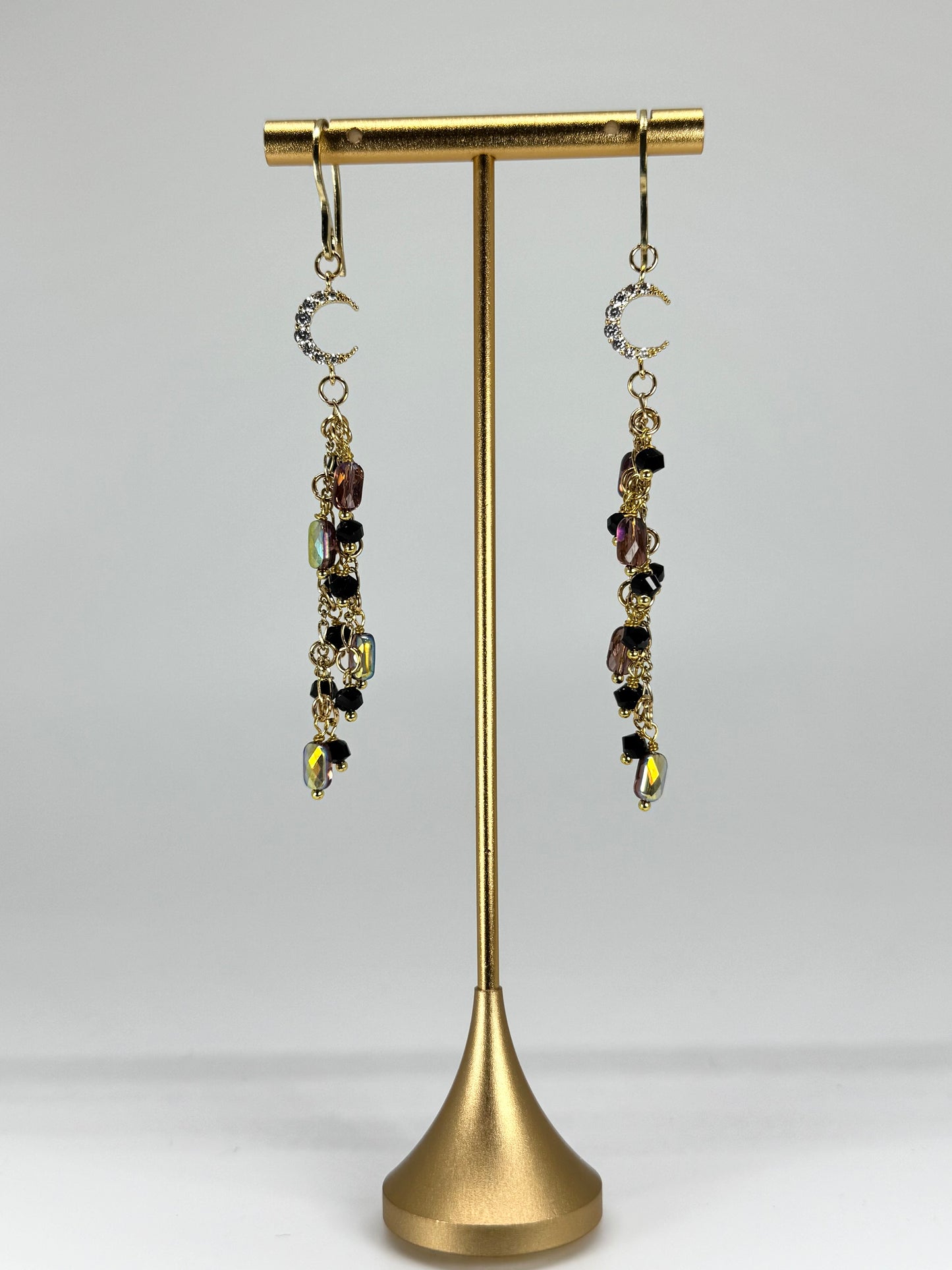 Pair of dangling earrings on a gold earring stand against a white background