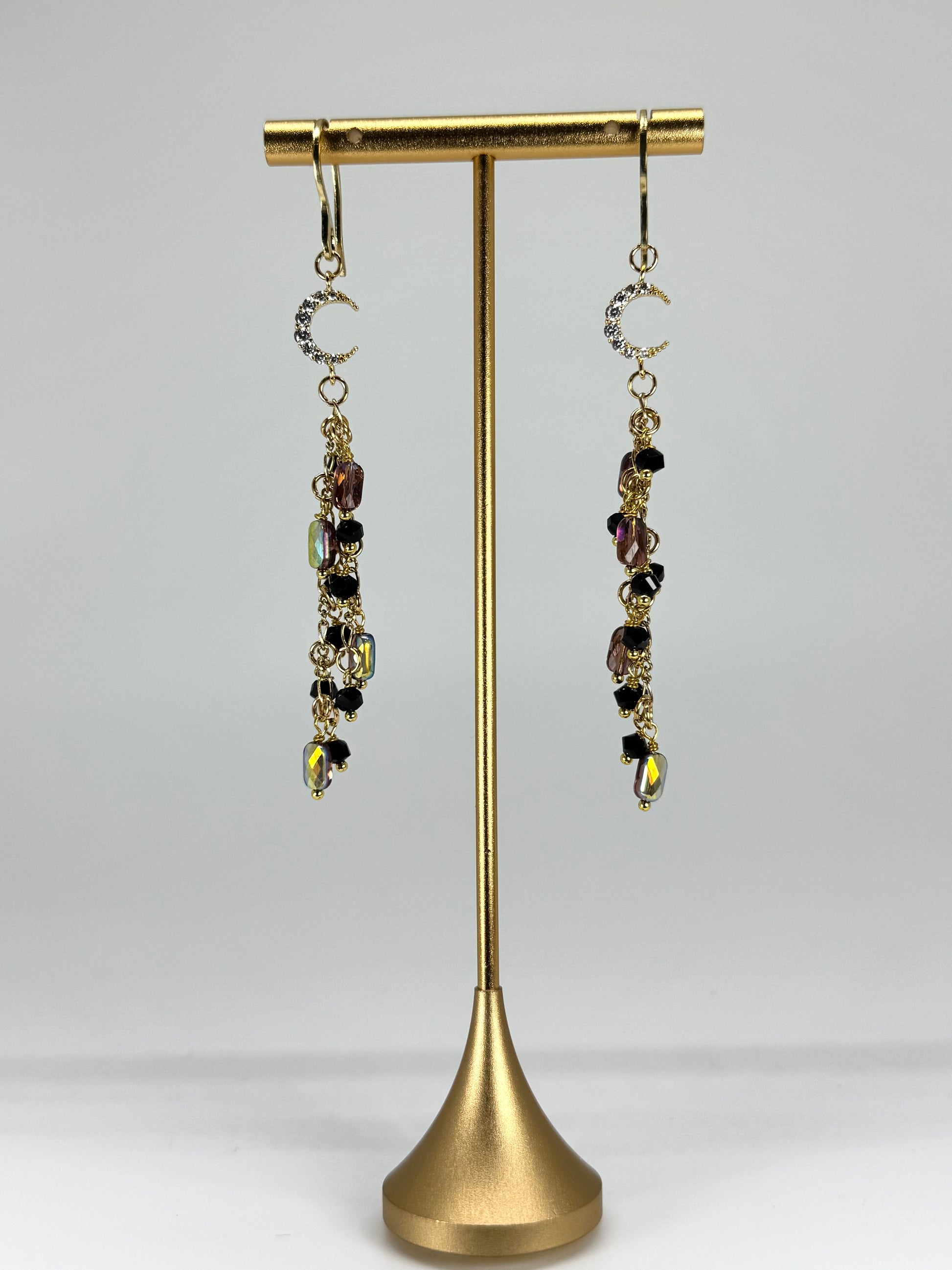 Pair of dangling earrings on a gold earring stand against a white background
