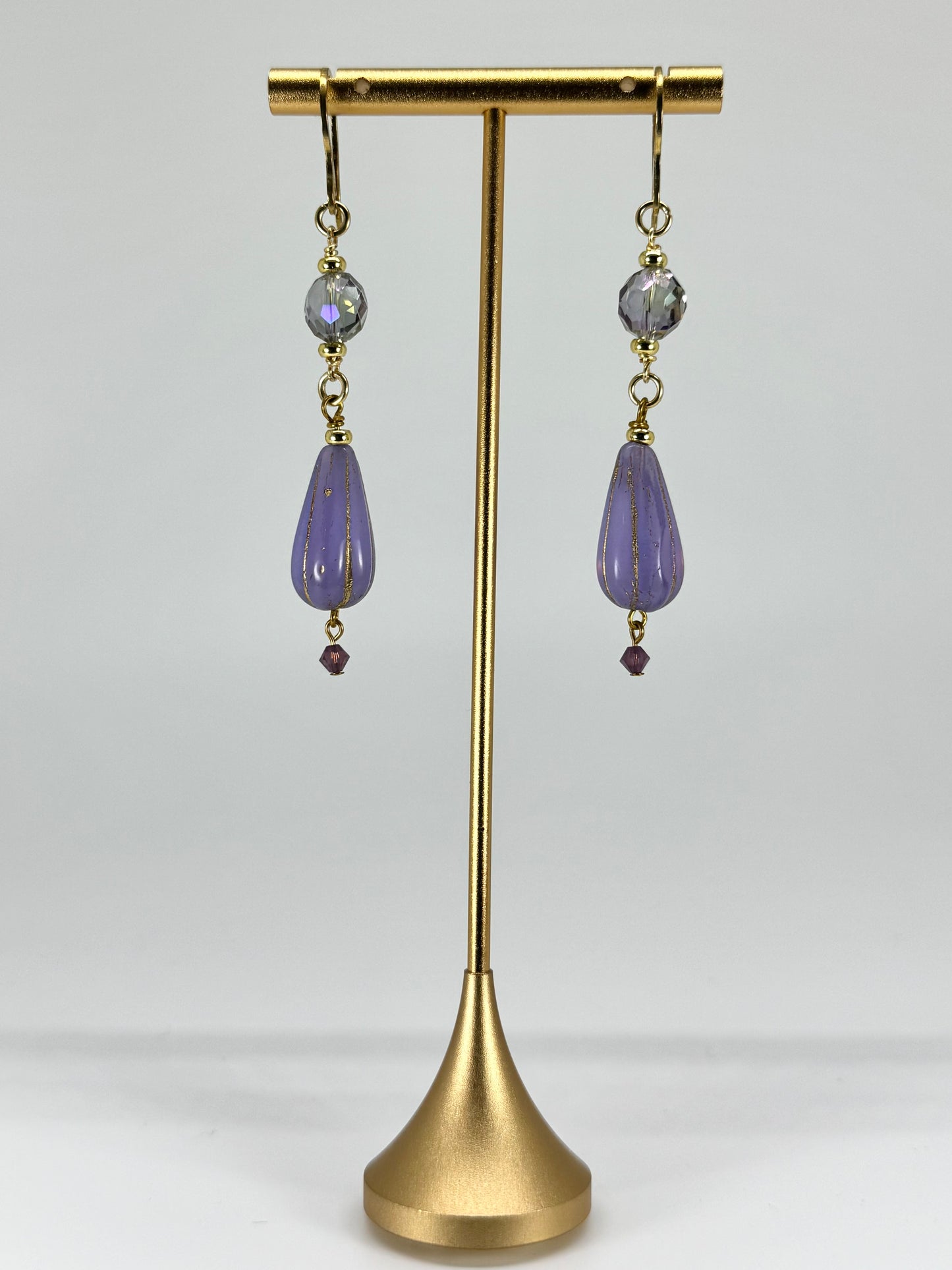 Purple teardrop earrings on a gold earring stand against a white background