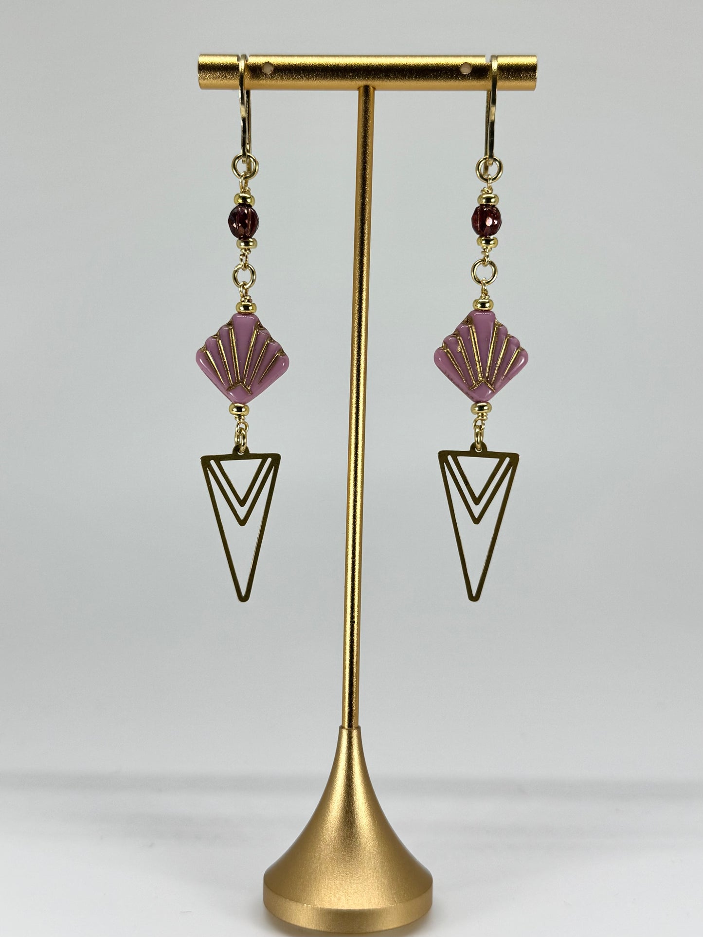 Pair of earrings with purple and gold design on a gold stand against a white background