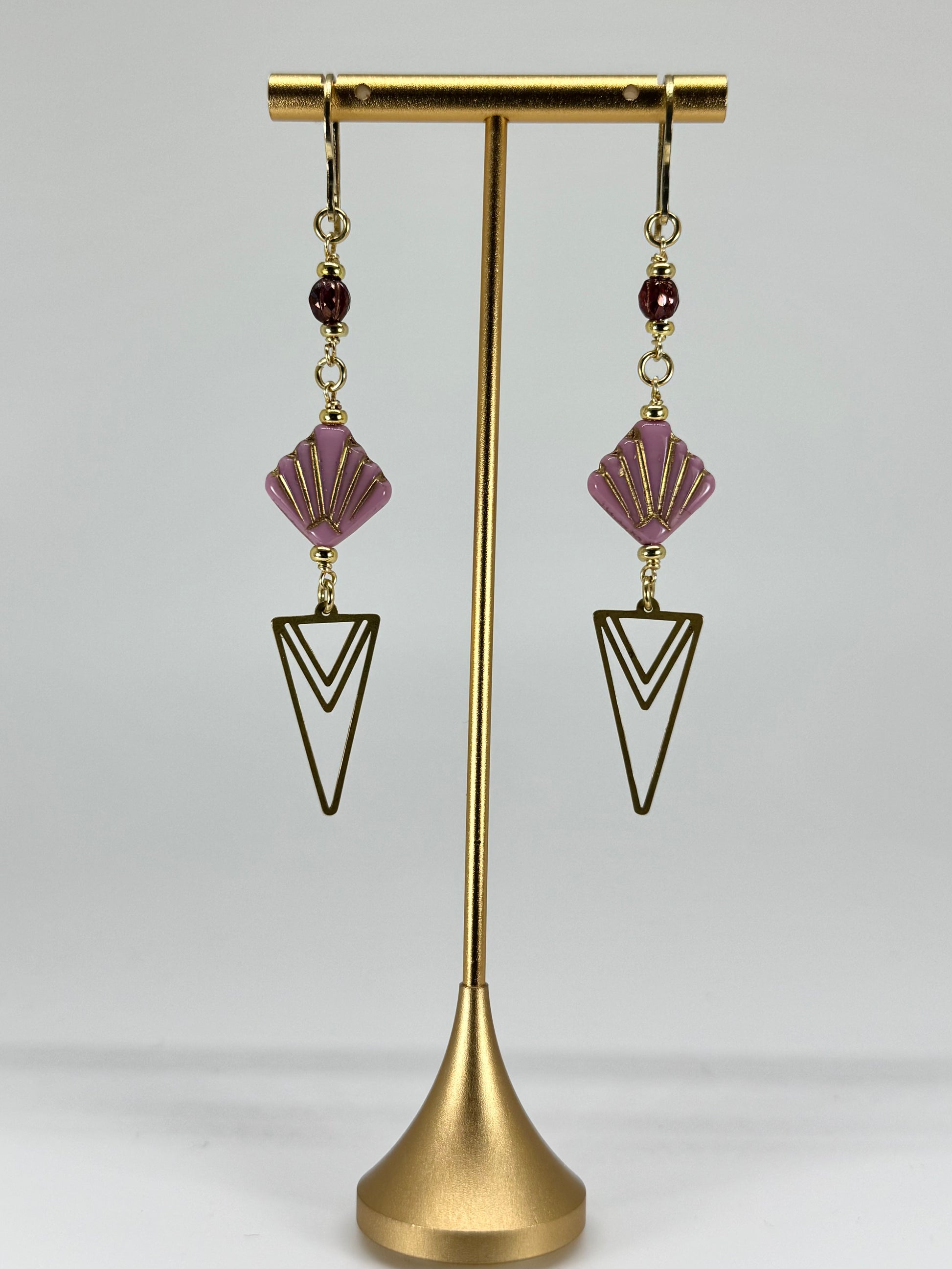Pair of earrings with purple and gold design on a gold stand against a white background