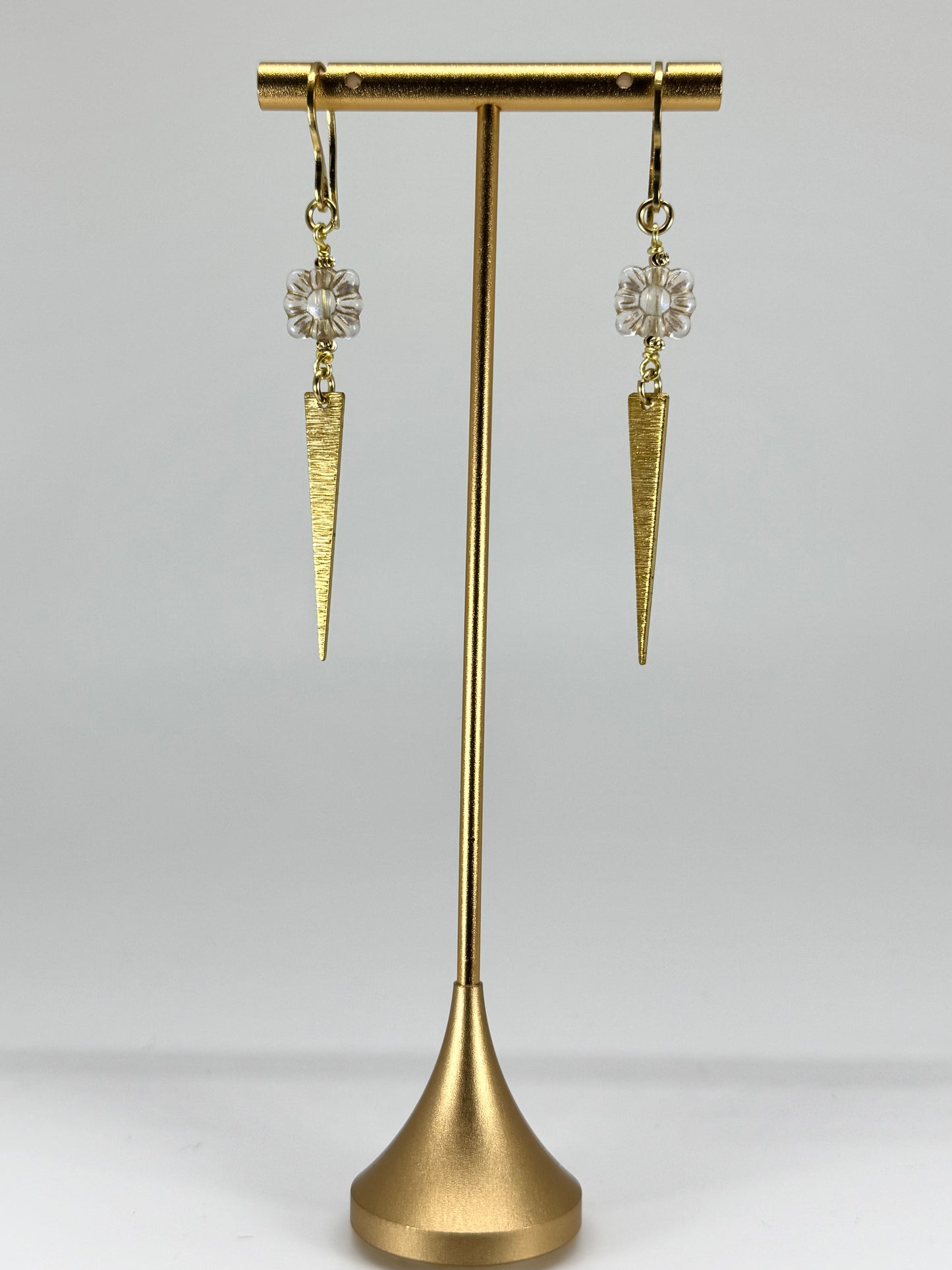 Gold earrings with cone-shaped designs on a gold stand against a gray background