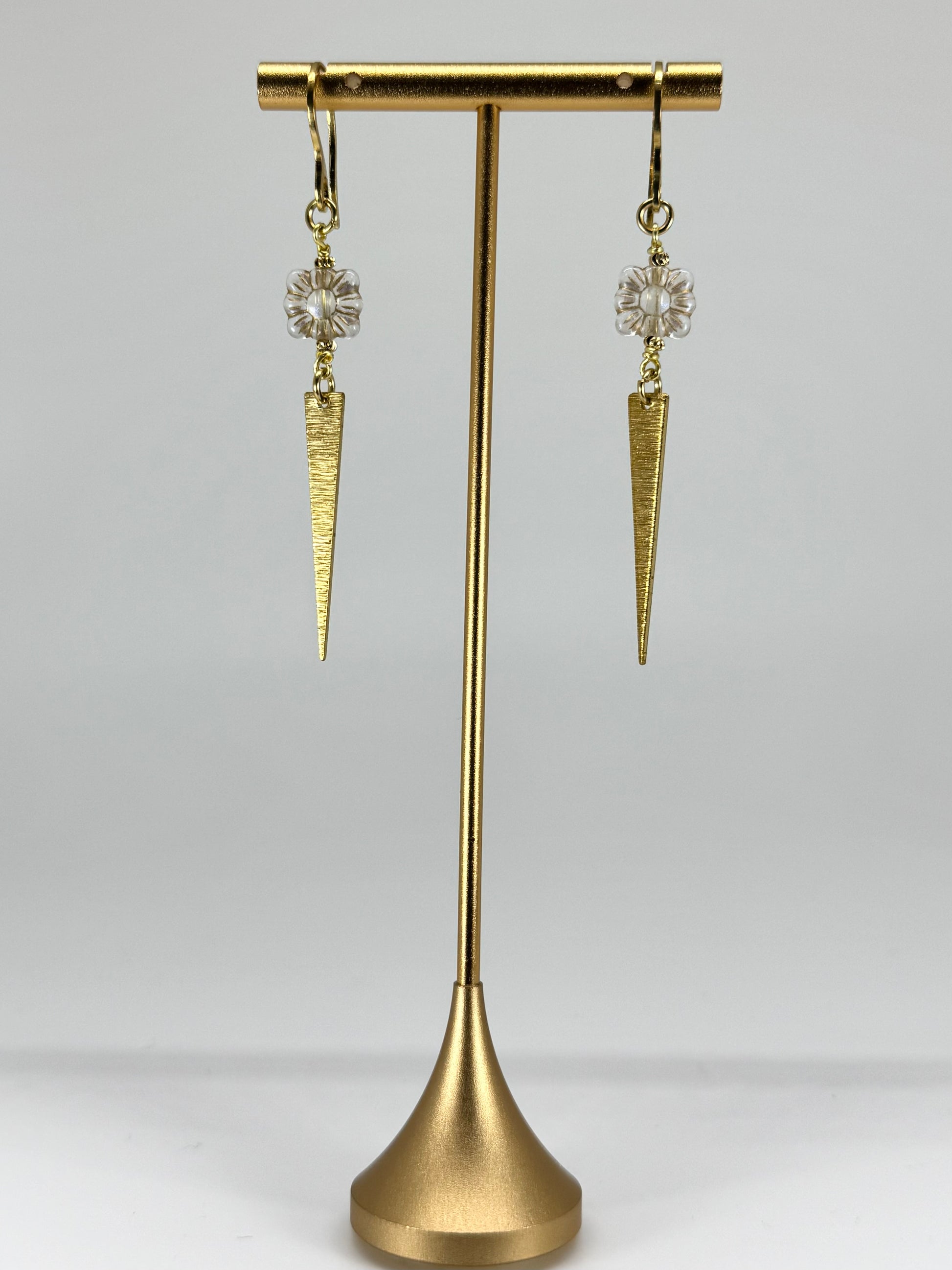 Gold earrings with cone-shaped designs on a gold stand against a gray background