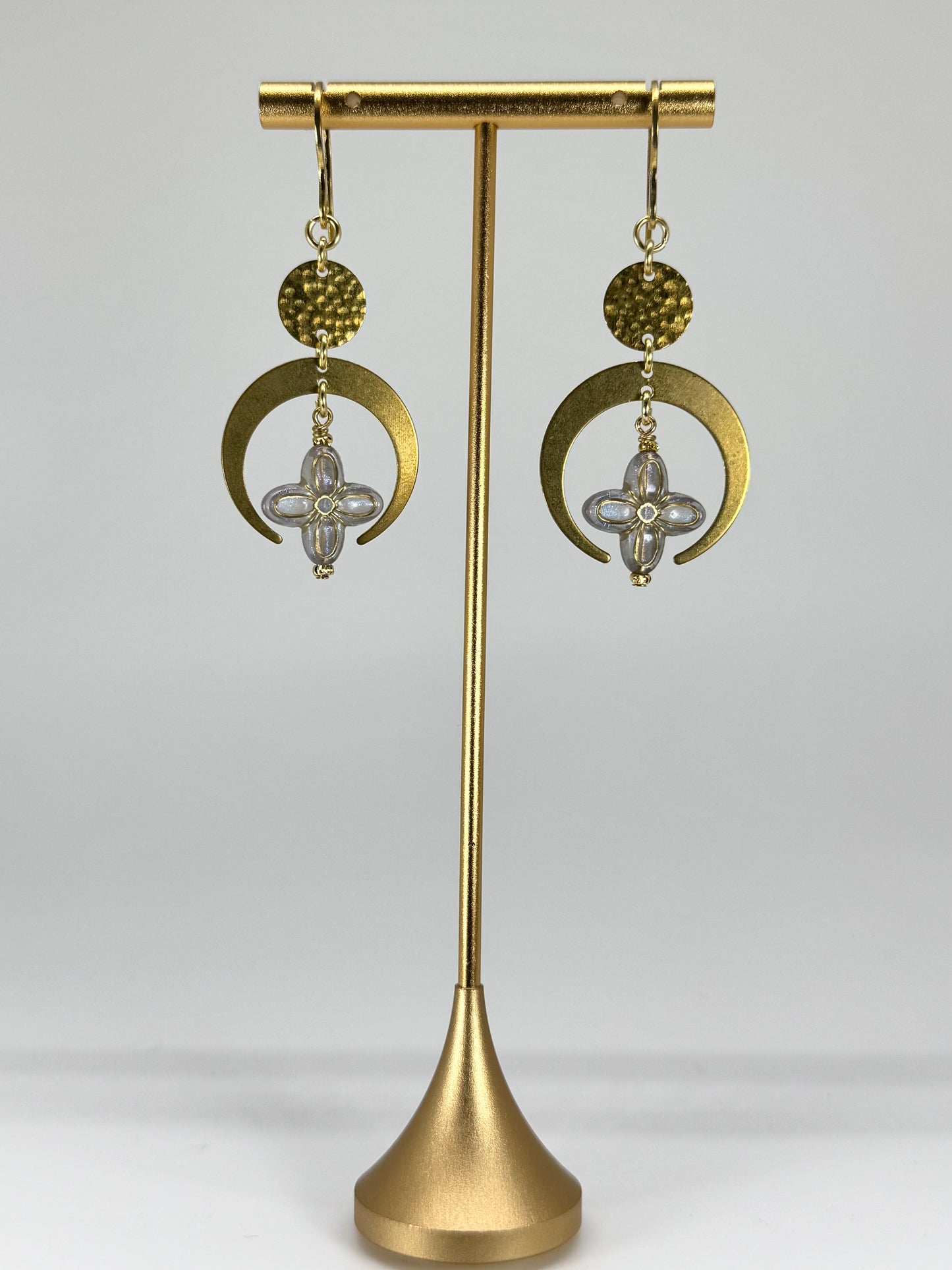 Gold earrings on a gold stand against a white background
