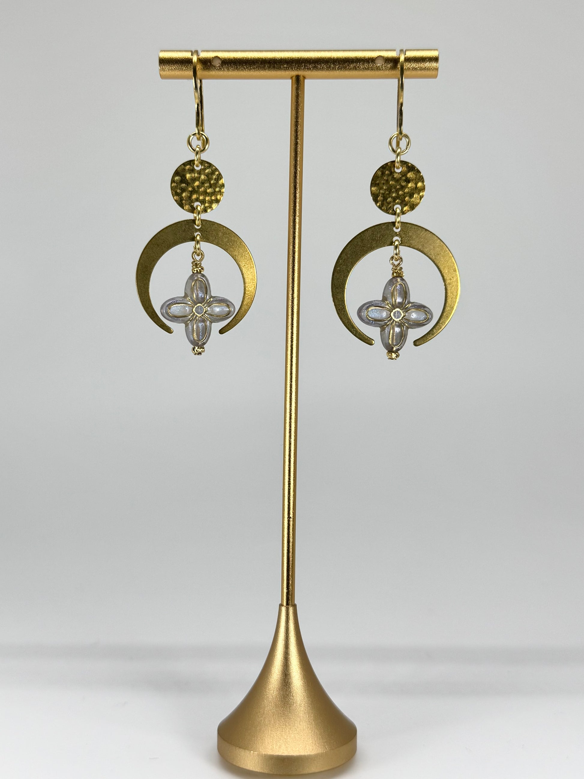 Gold earrings on a gold stand against a white background
