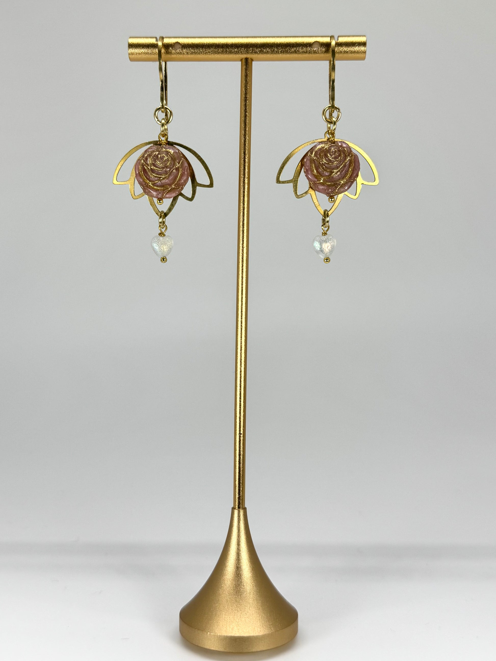 Gold earrings on a matching stand against a light gray background