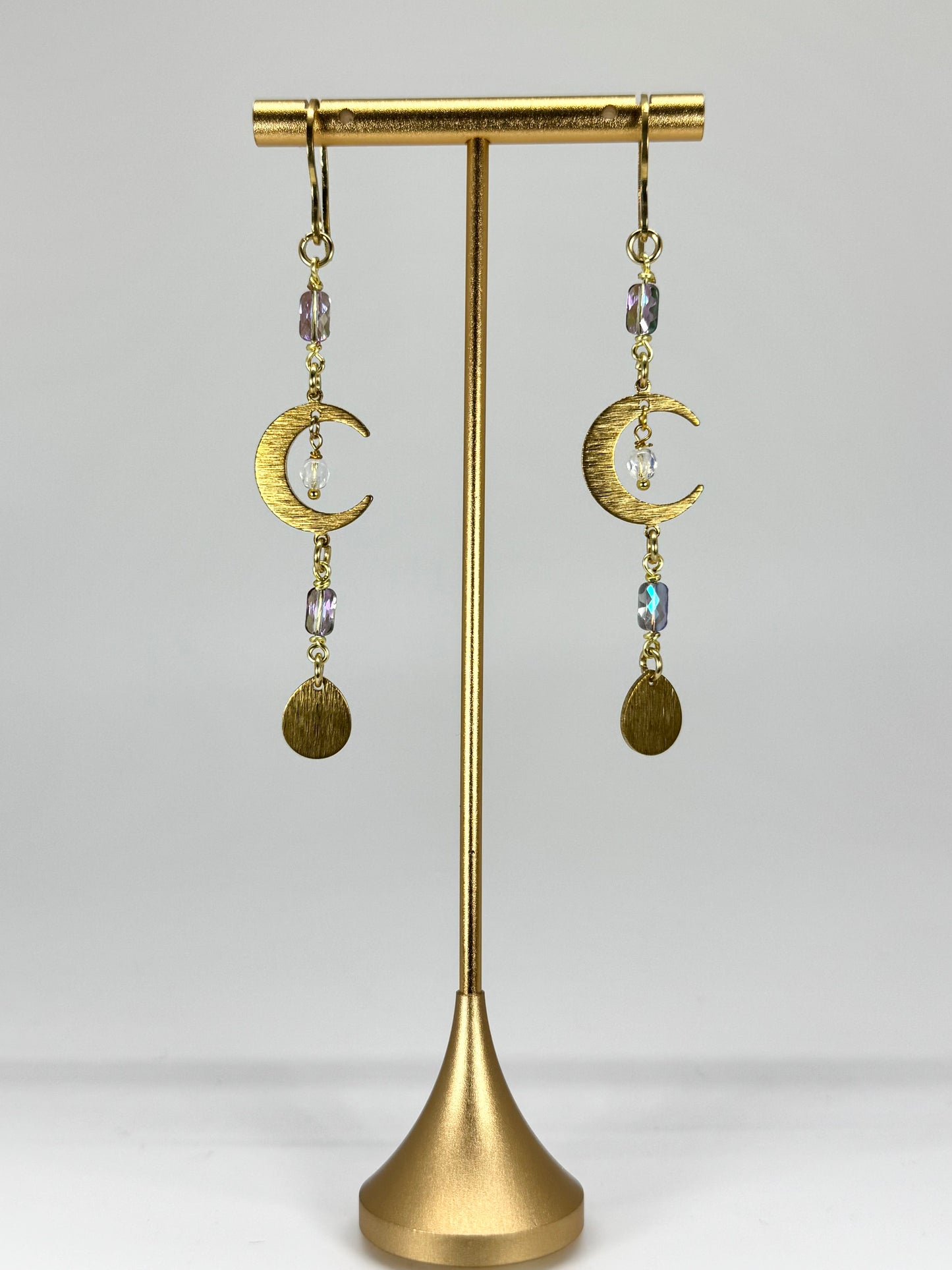 Gold earrings with moon designs on a gold stand against a white background