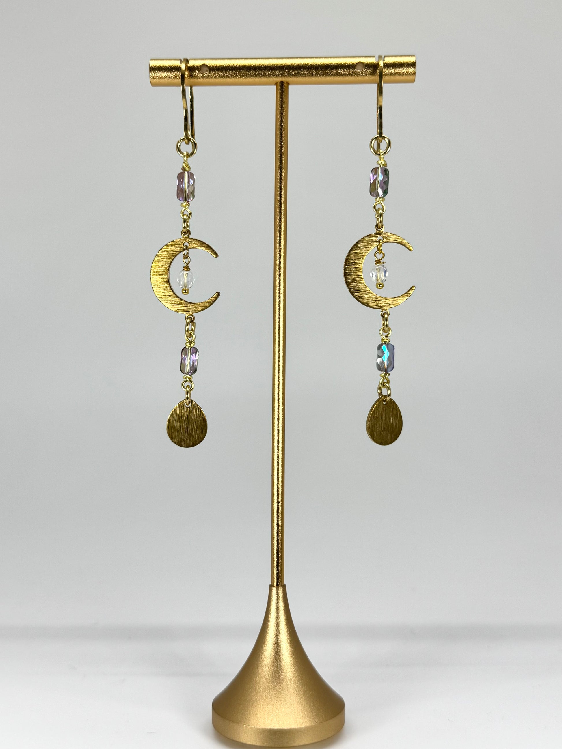 Gold earrings with moon designs on a gold stand against a white background