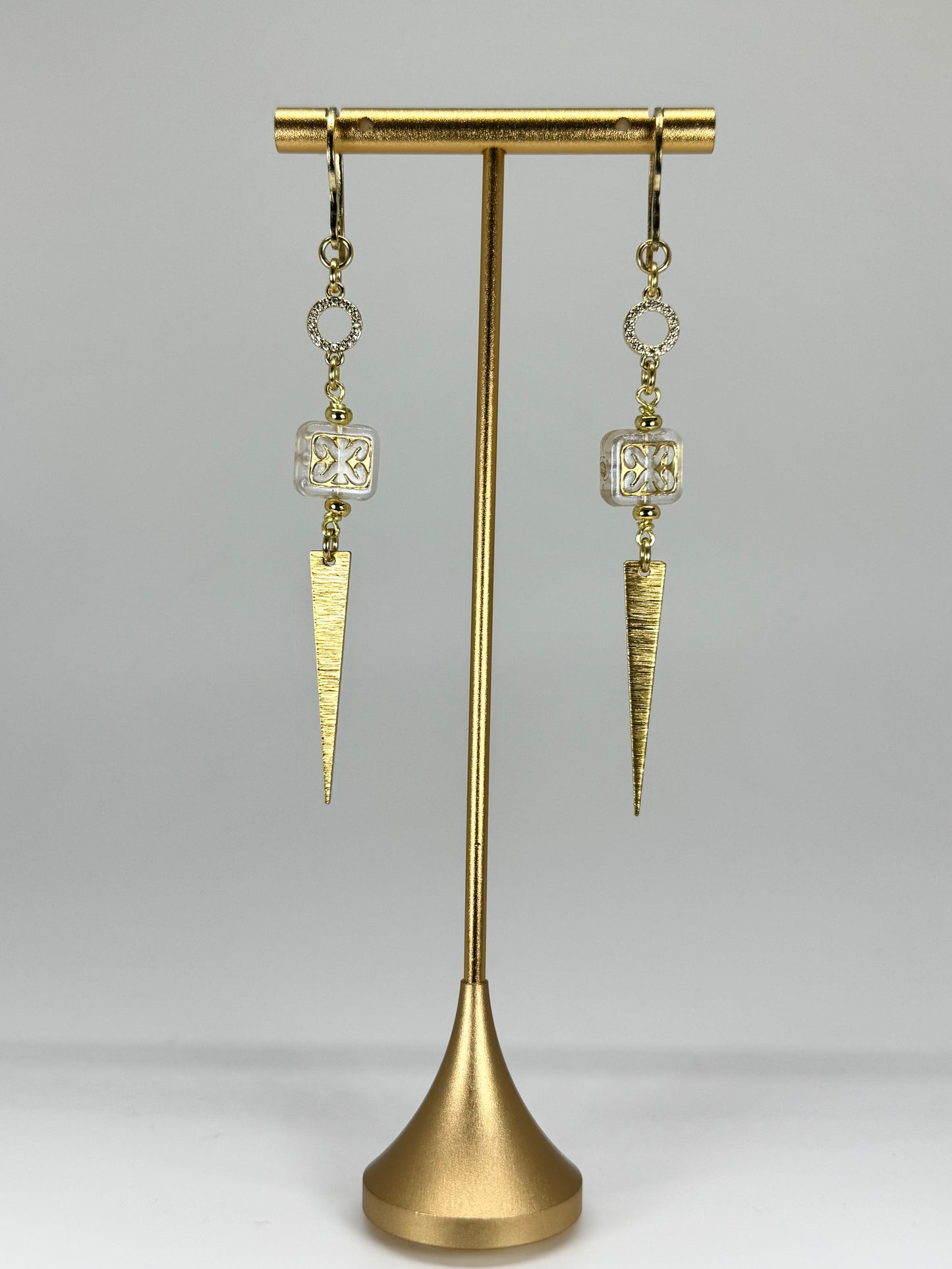 Pair of gold earrings on a stand against a gray background