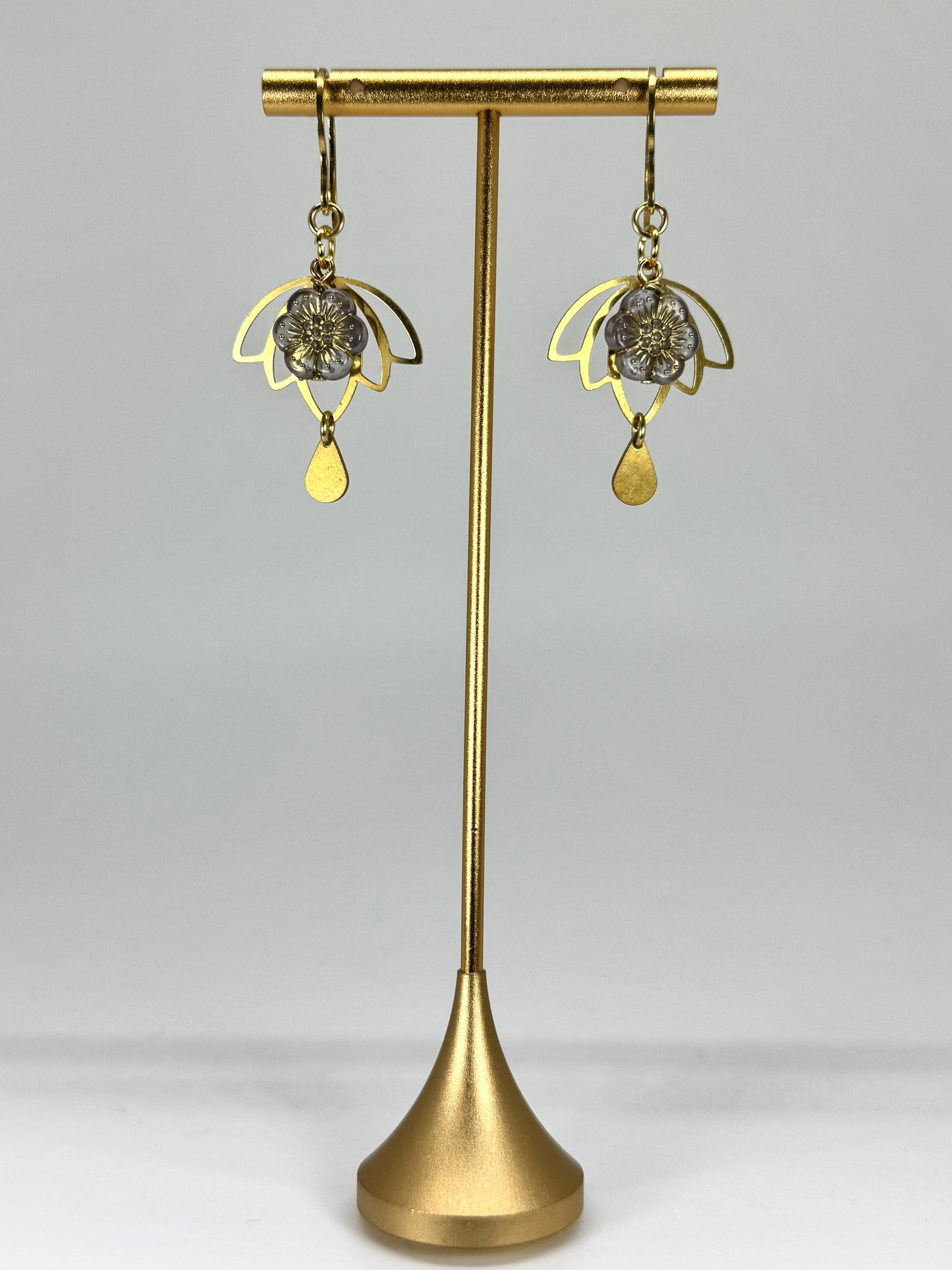 Gold earrings on a gold stand against a gray background