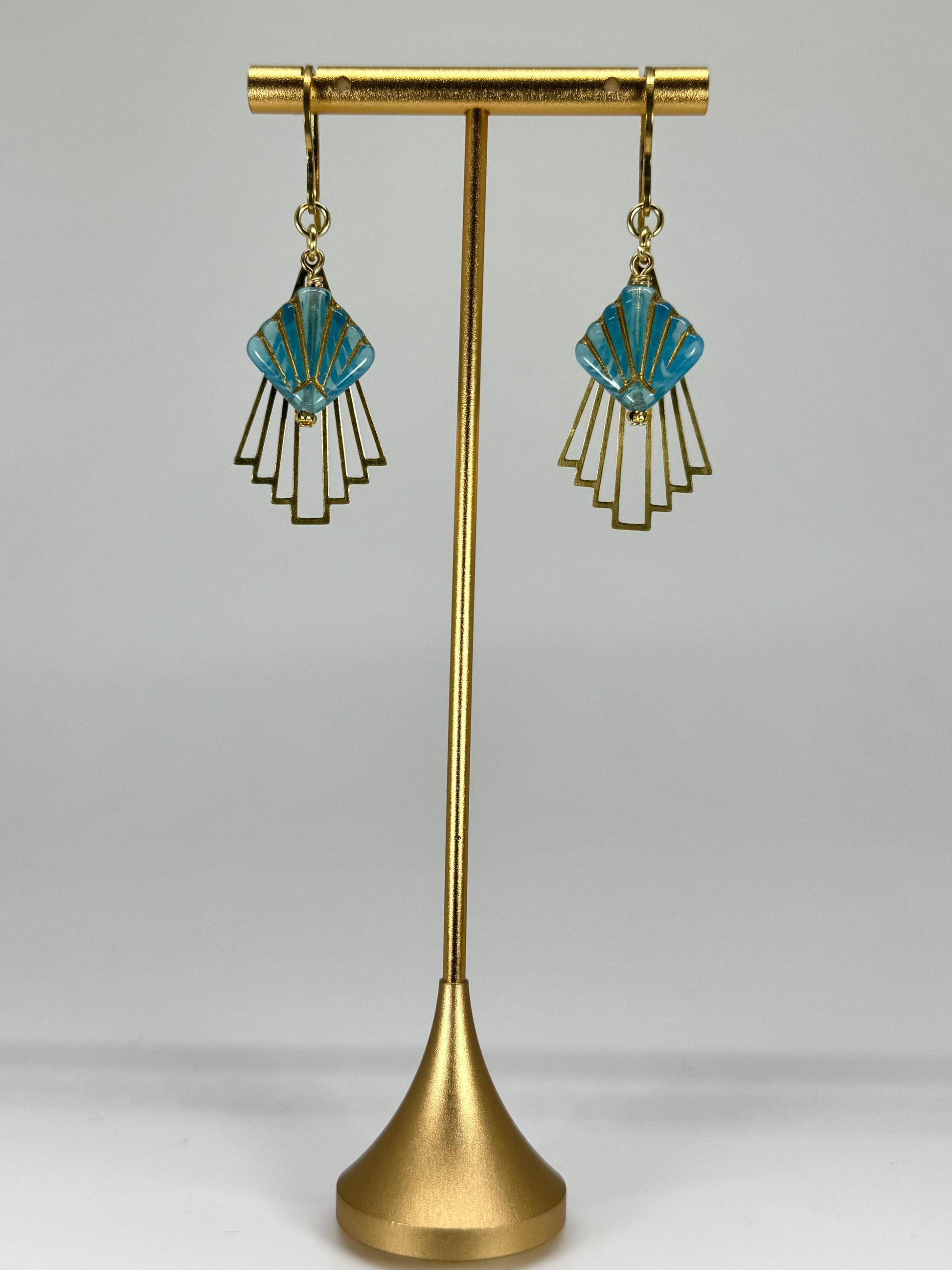 Pair of blue and gold earrings on a gold stand against a gray background