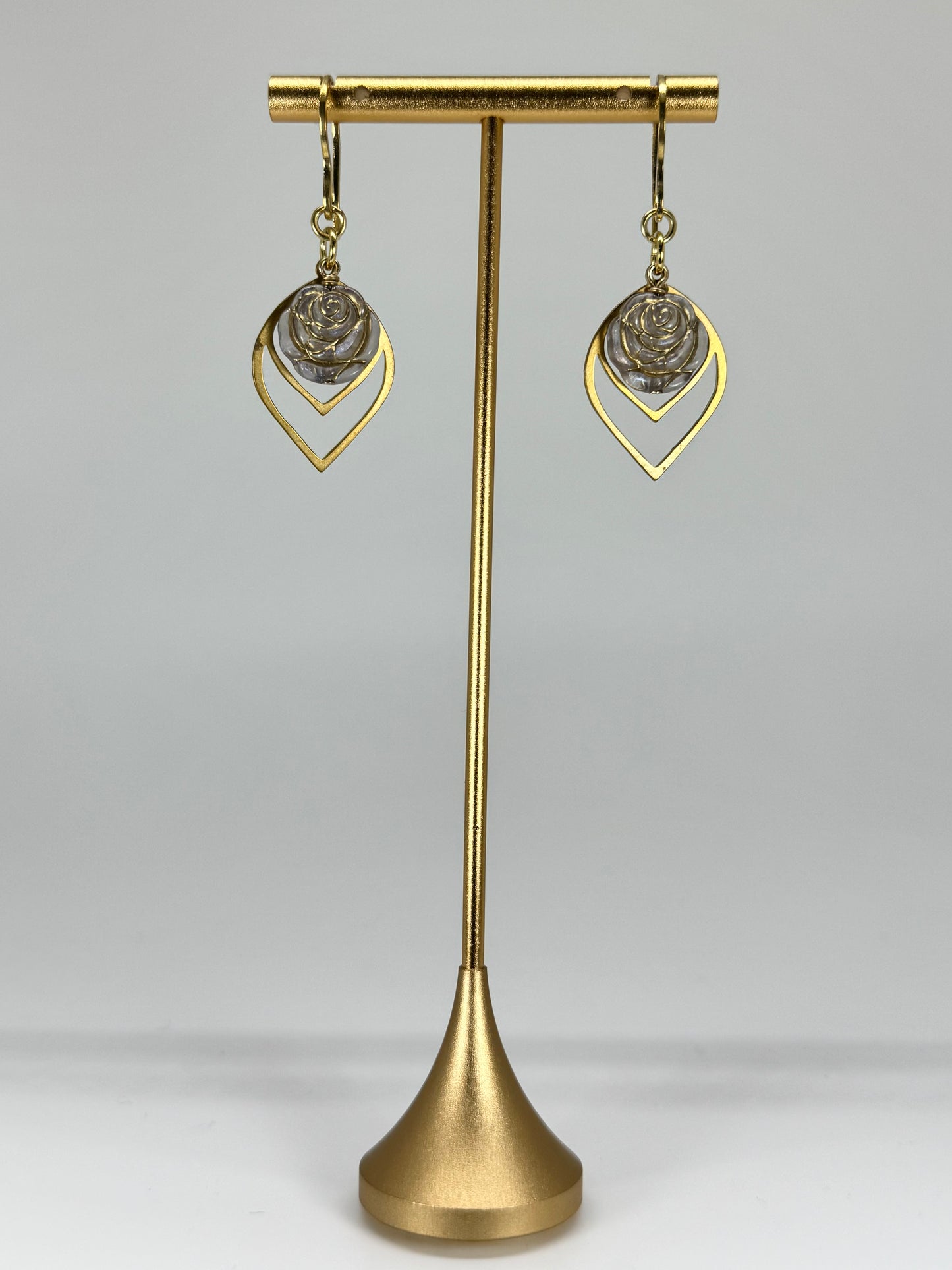 Gold earrings on a gold stand against a gray background