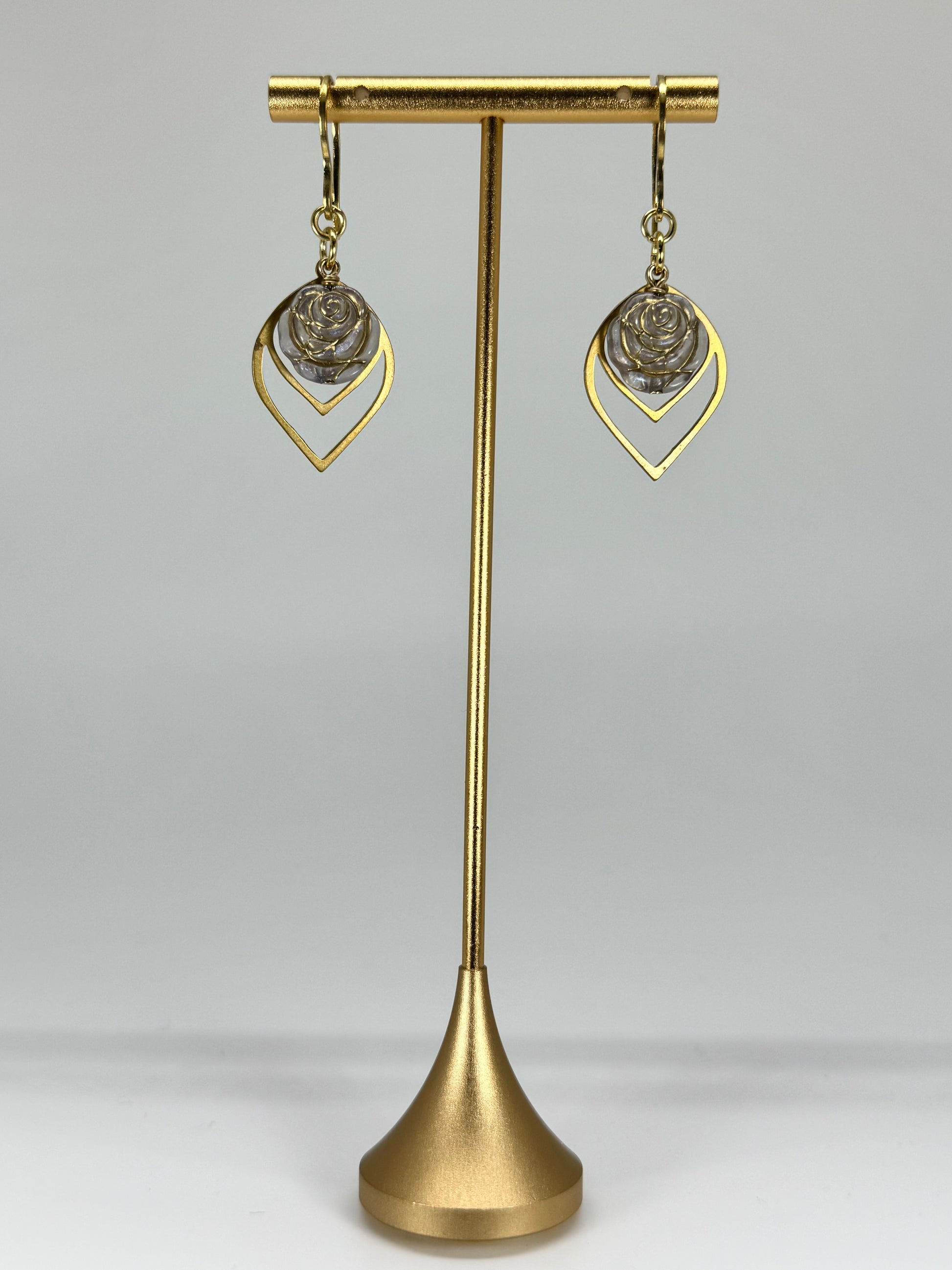 Gold earrings on a gold stand against a gray background