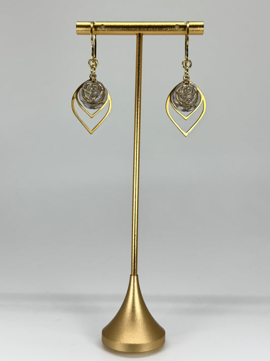 Gold earrings on a gold stand against a gray background