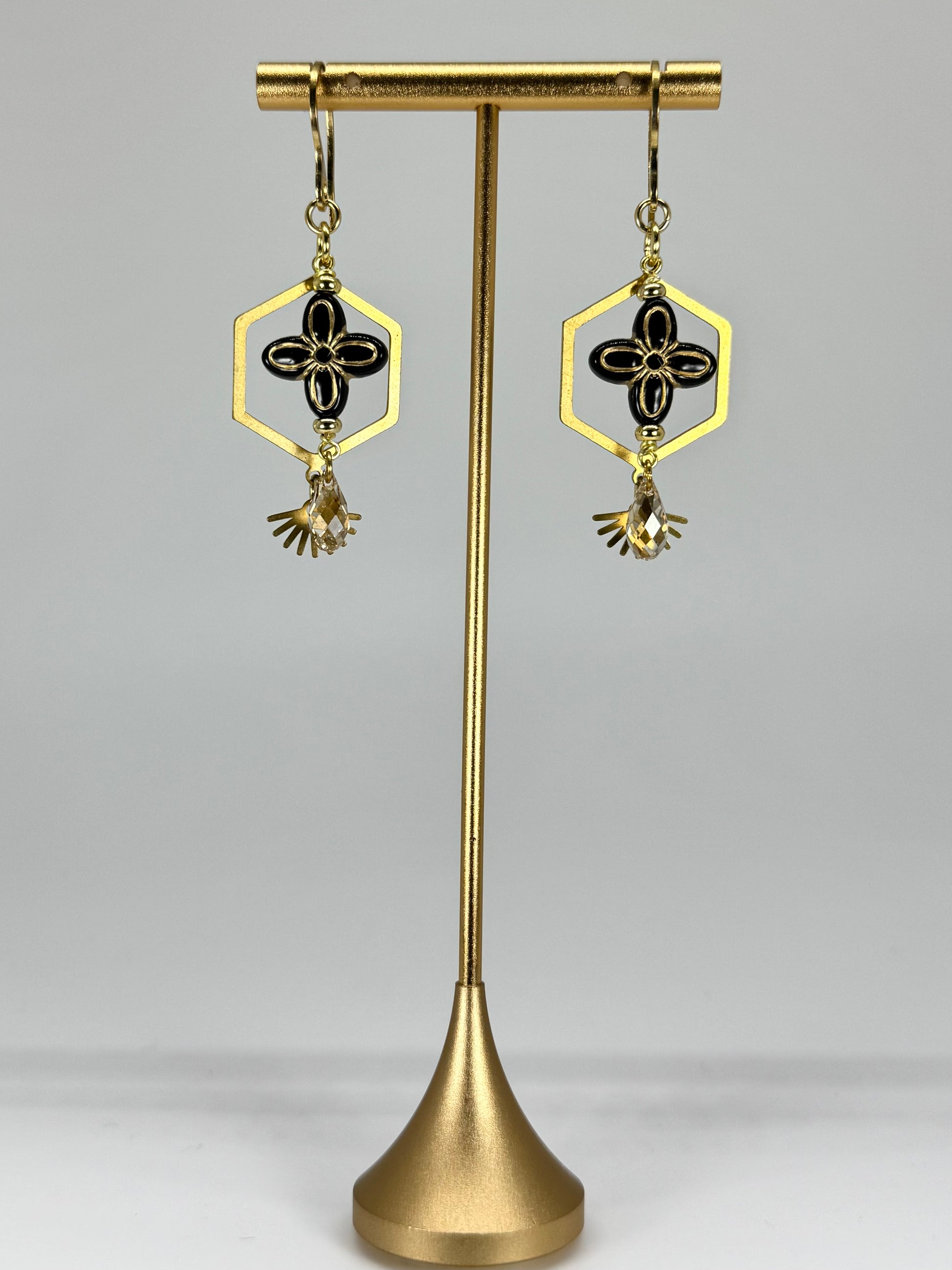 Gold and black earrings on a gold stand against a gray background