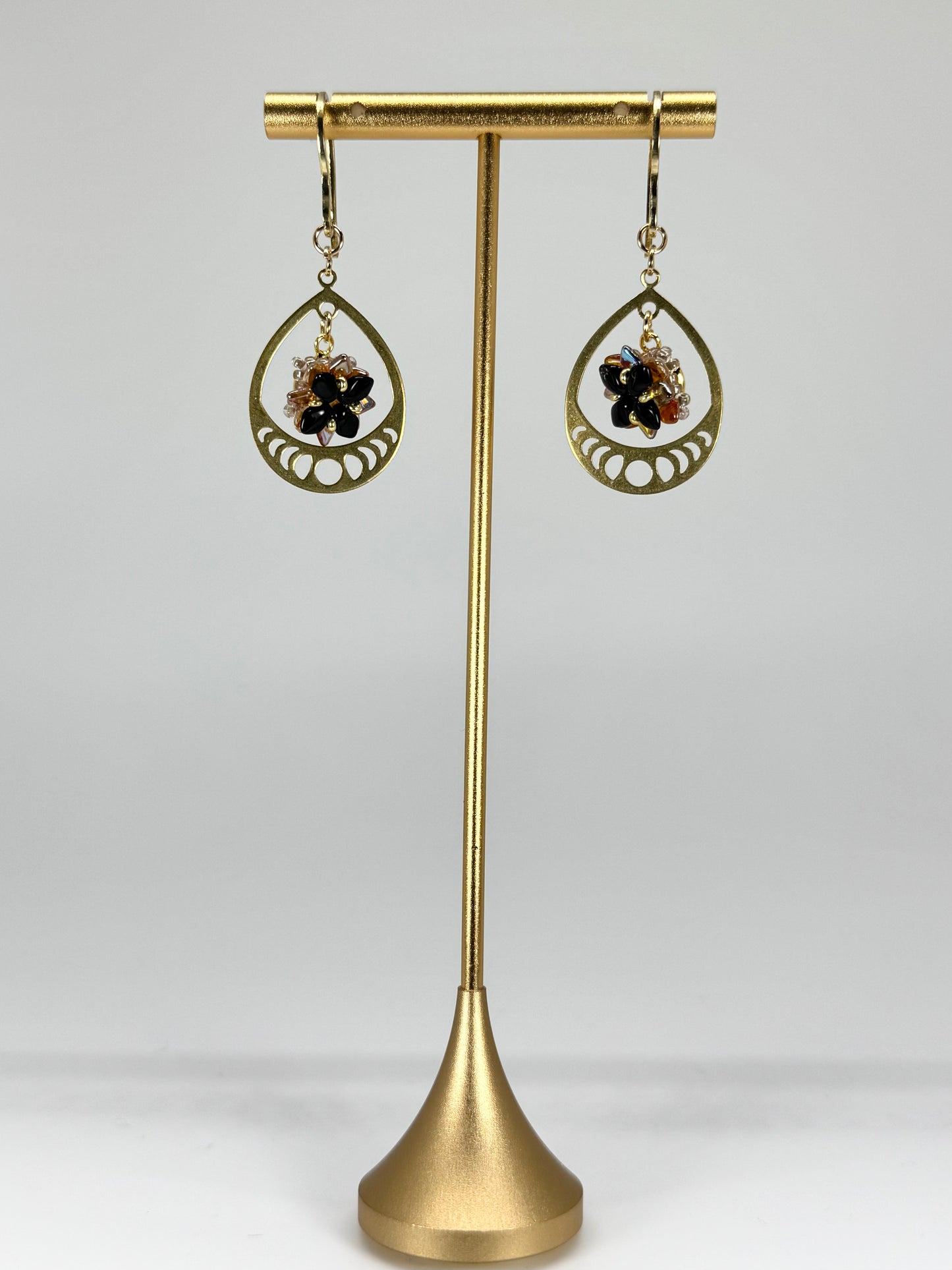 Gold earrings with black stones on a gold stand against a white background
