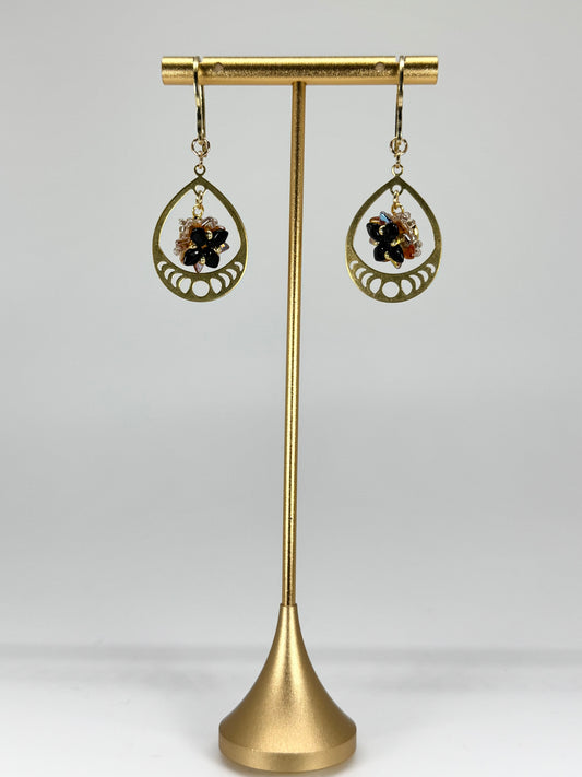 Gold earrings with black stones on a gold stand against a white background