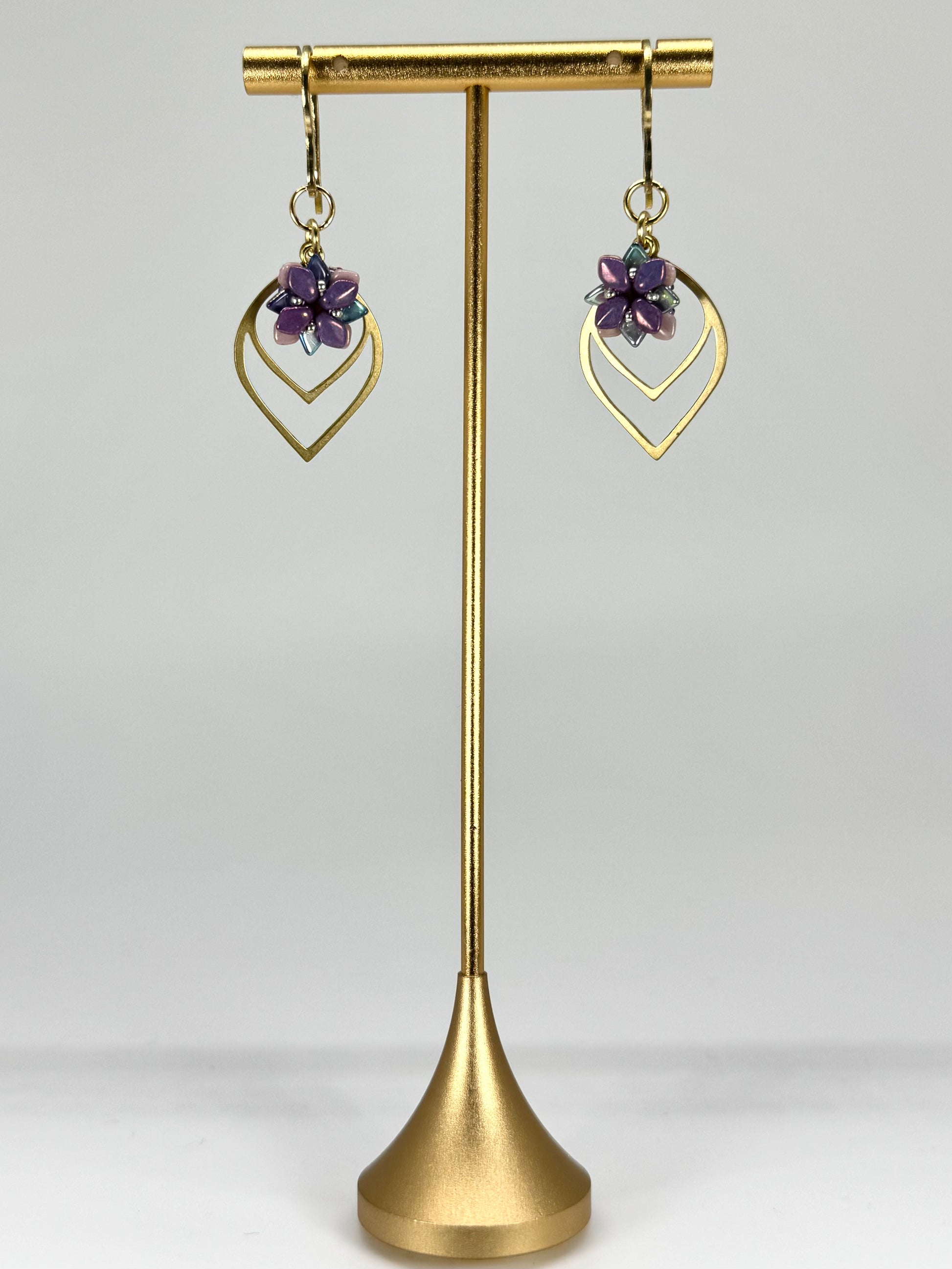 Gold earrings with purple stones on a gold stand against a white background