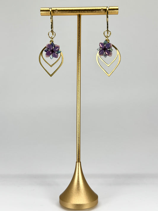 Gold earrings with purple stones on a gold stand against a white background