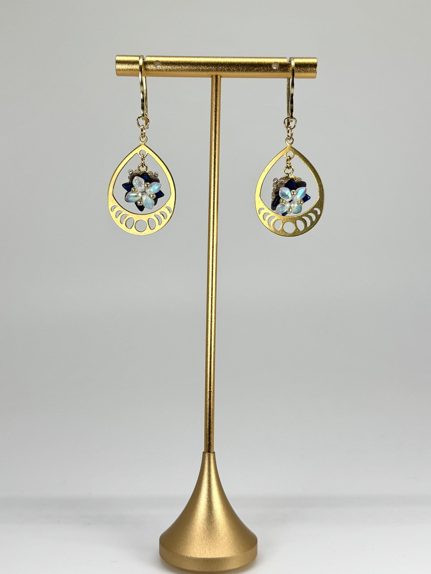 Gold teardrop earrings on a gold stand against a gray background