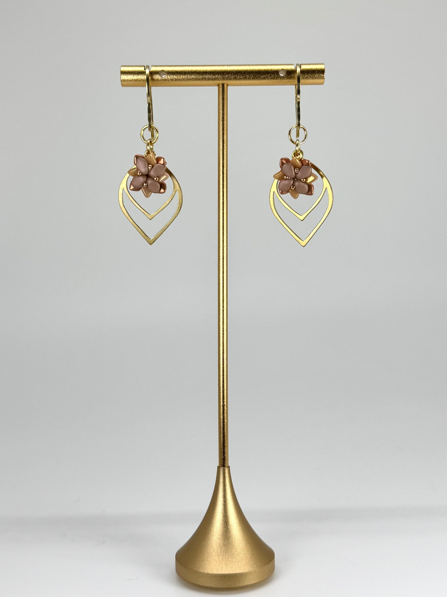 Gold earrings on a gold stand against a gray background