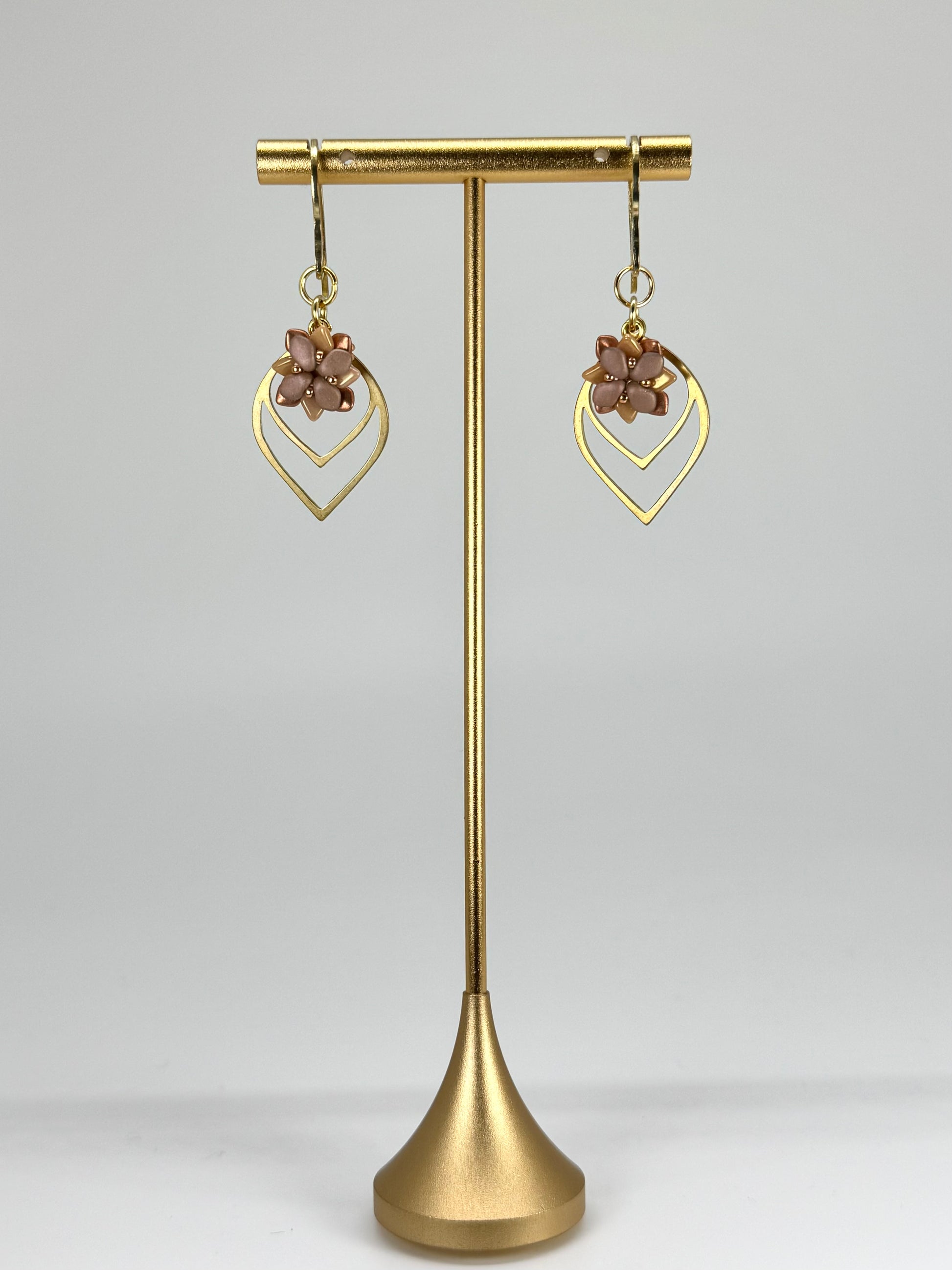 Gold earrings on a gold stand against a gray background