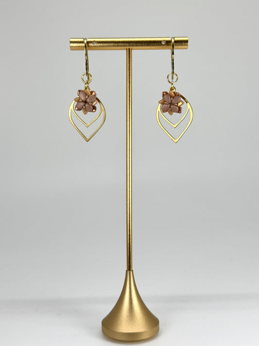 Gold earrings on a gold stand against a gray background