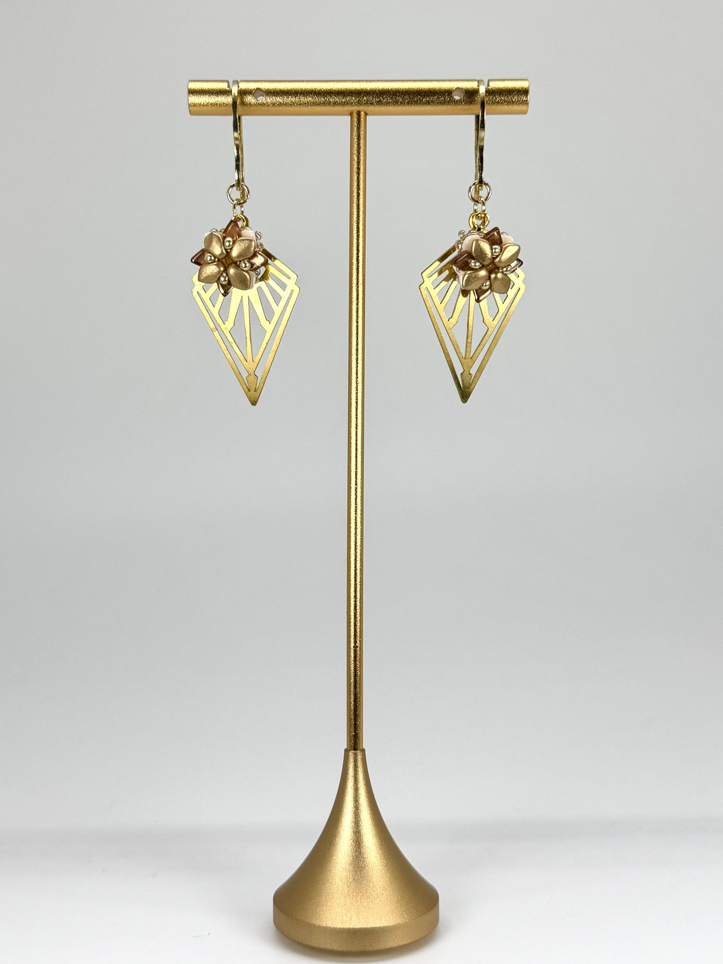 Gold earrings on a gold stand against a gray background