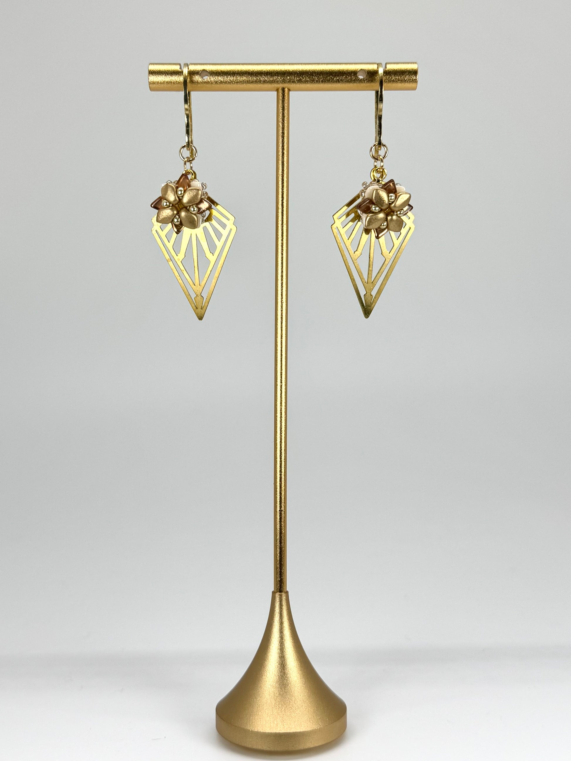 Gold earrings on a gold stand against a gray background