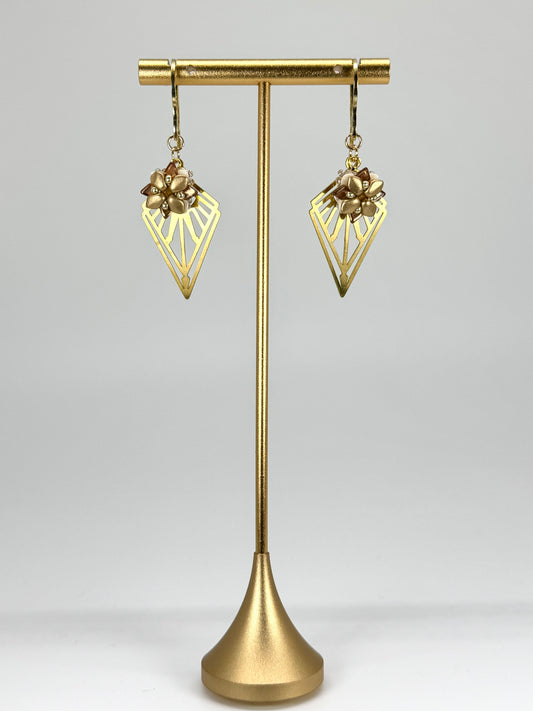 Gold earrings on a gold stand against a gray background