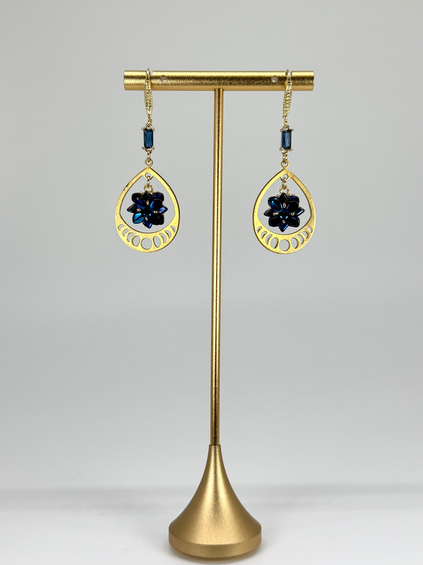 Gold earrings with black stones on a brass stand against a gray background