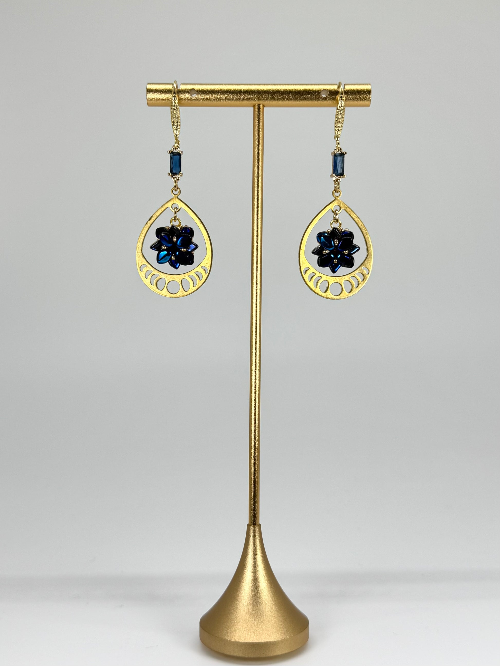 Gold earrings with black stones on a brass stand against a gray background