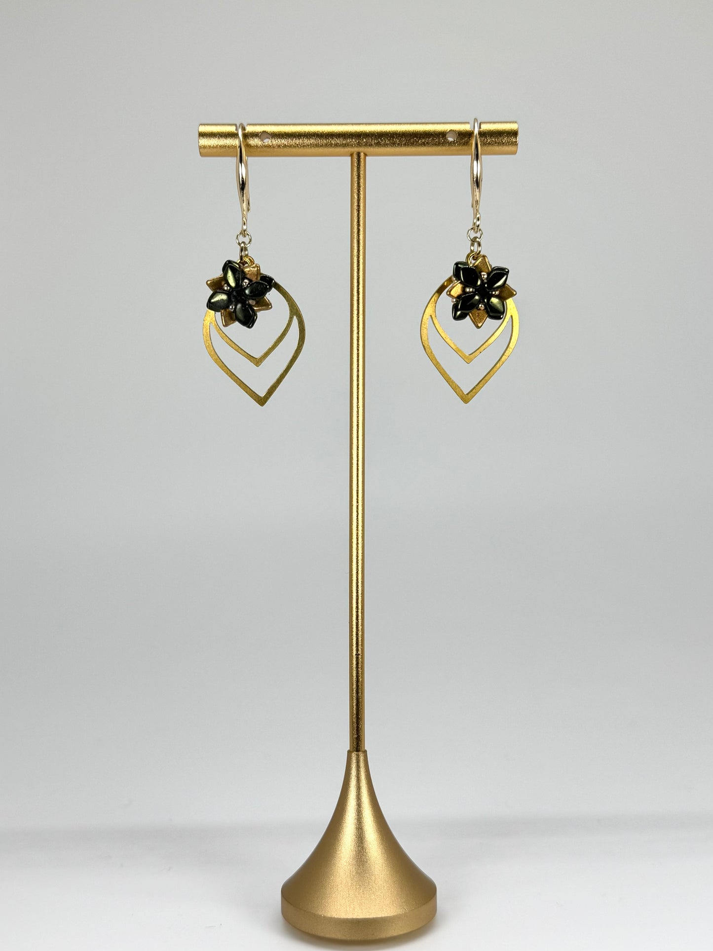 Gold earrings on a gold stand against a gray background