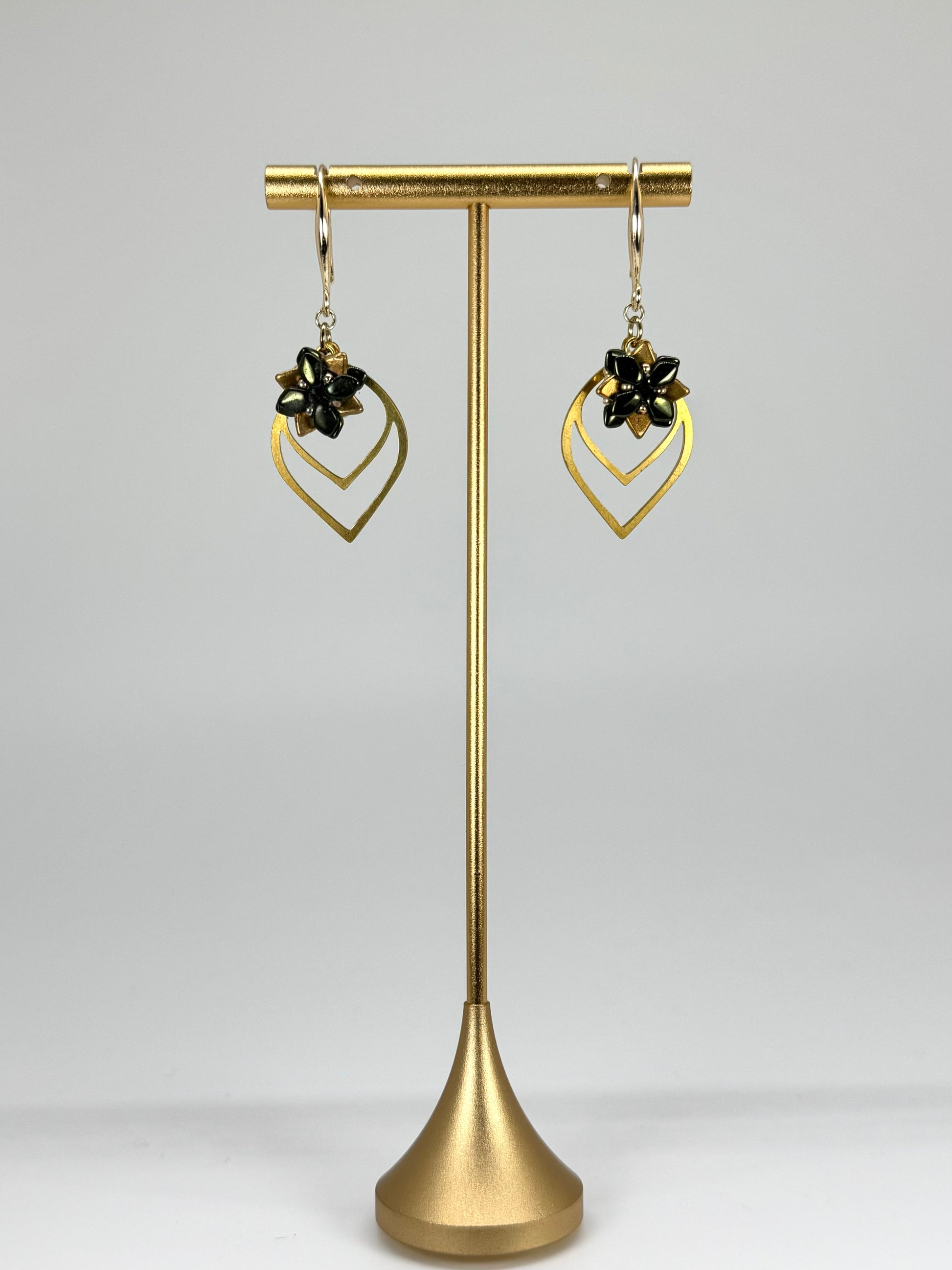 Gold earrings on a gold stand against a gray background