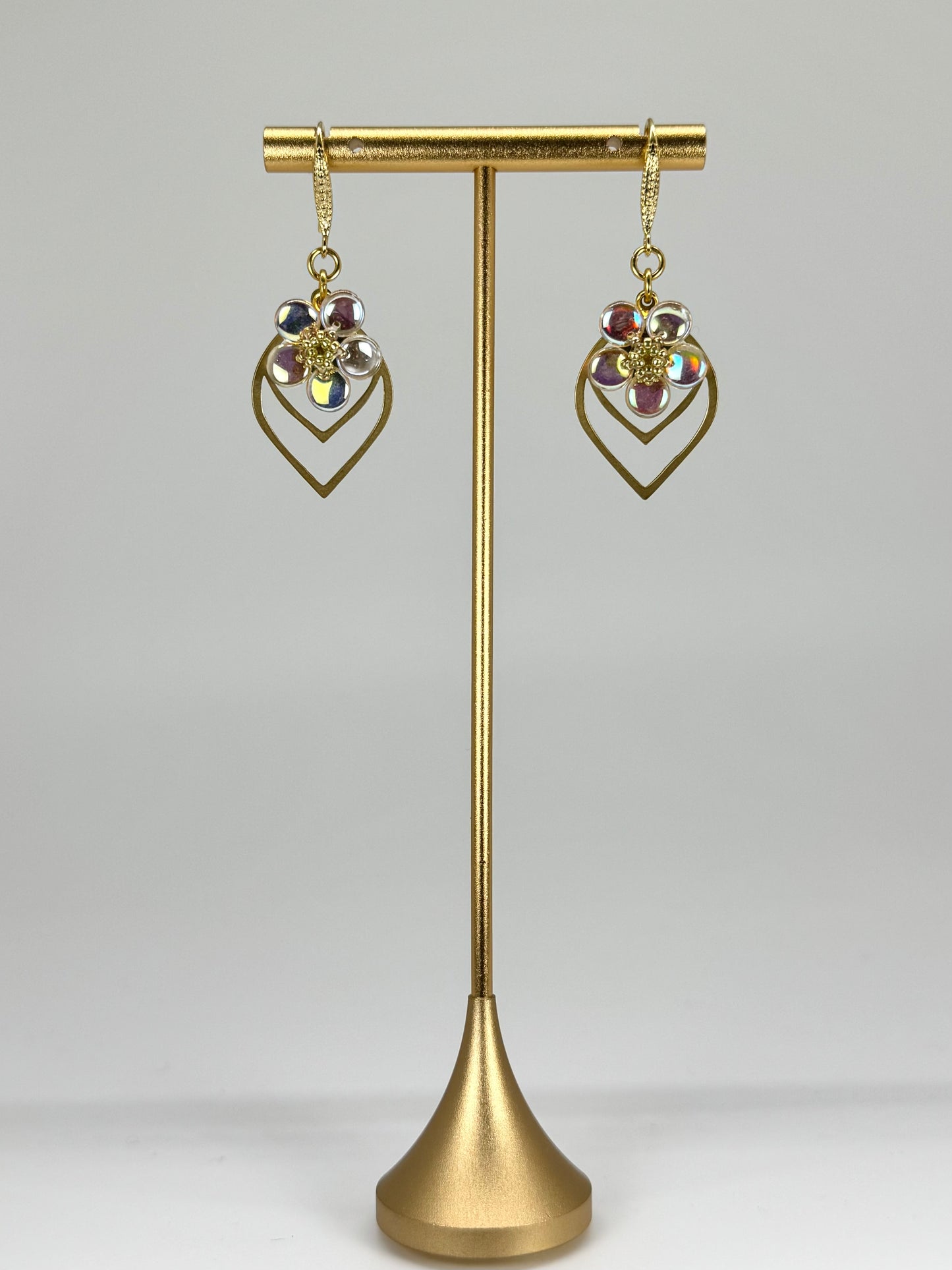 Gold earrings on a gold stand against a gray background
