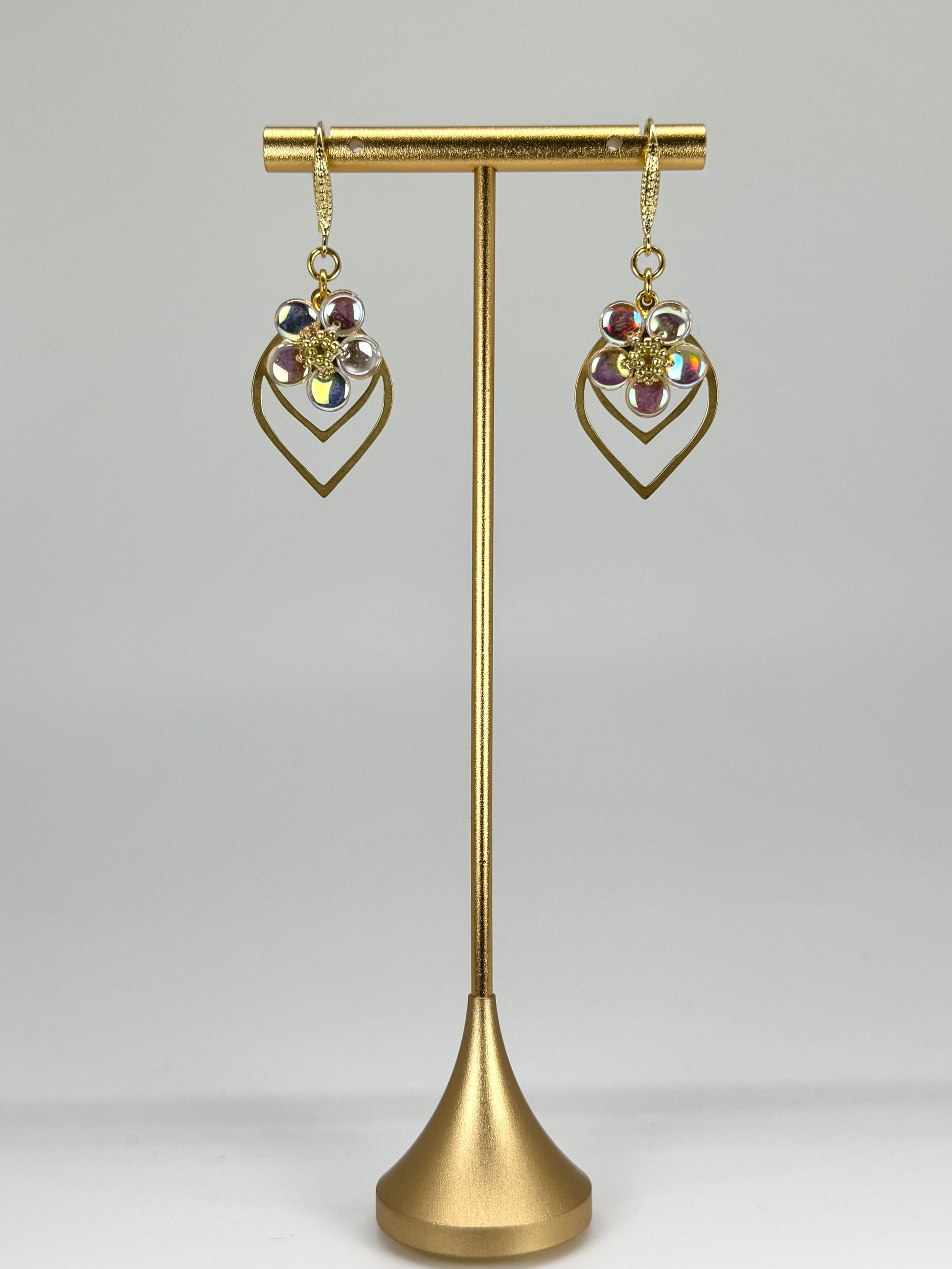 Gold earrings on a gold stand against a gray background